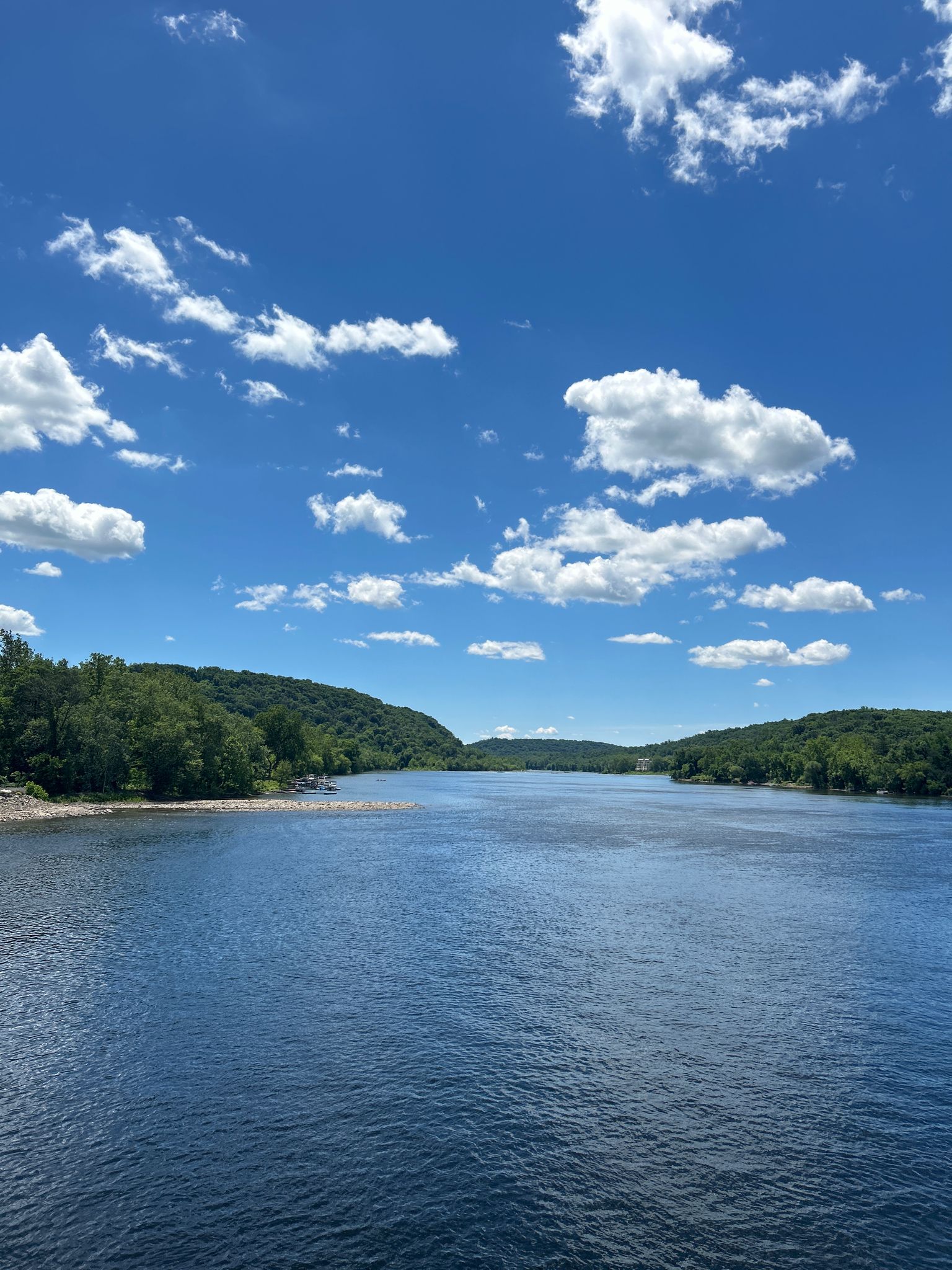 A wide river flows between lush green banks under a bright, cloudy sky. - New Hope-Lambertville Bridge – Stockton Inn loop from Ted Stiles Preserve at Baldpate Mountain