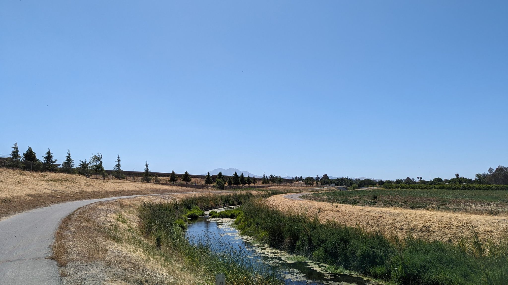 Paved path next to a narrow stream, dry grass, clear blue sky. - Marsh Creek Regional Trail