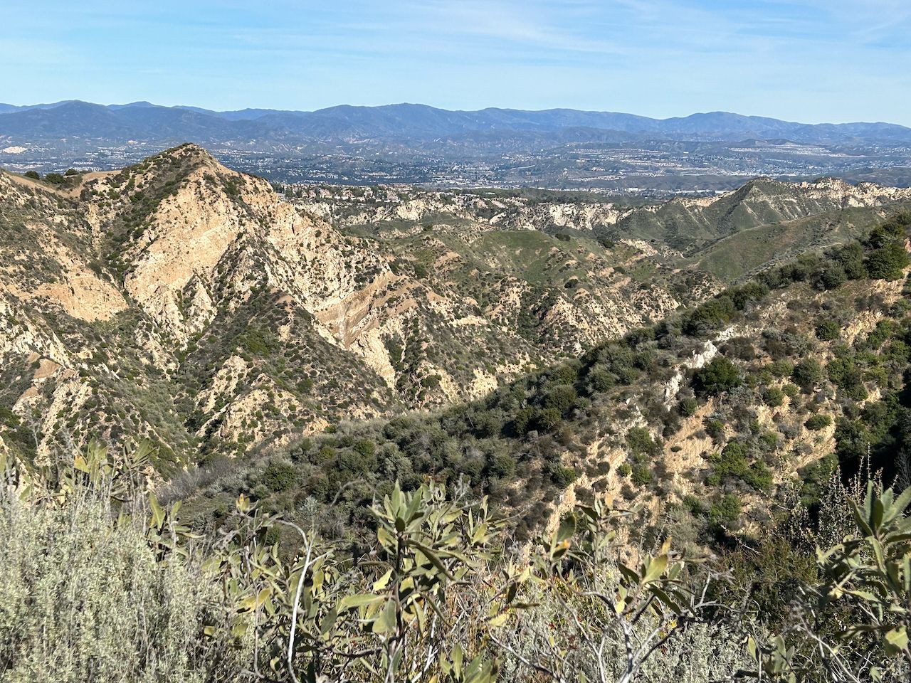 Rugged, brush-covered mountains overlooking a distant city on a clear day. - Pico Canyon Loop