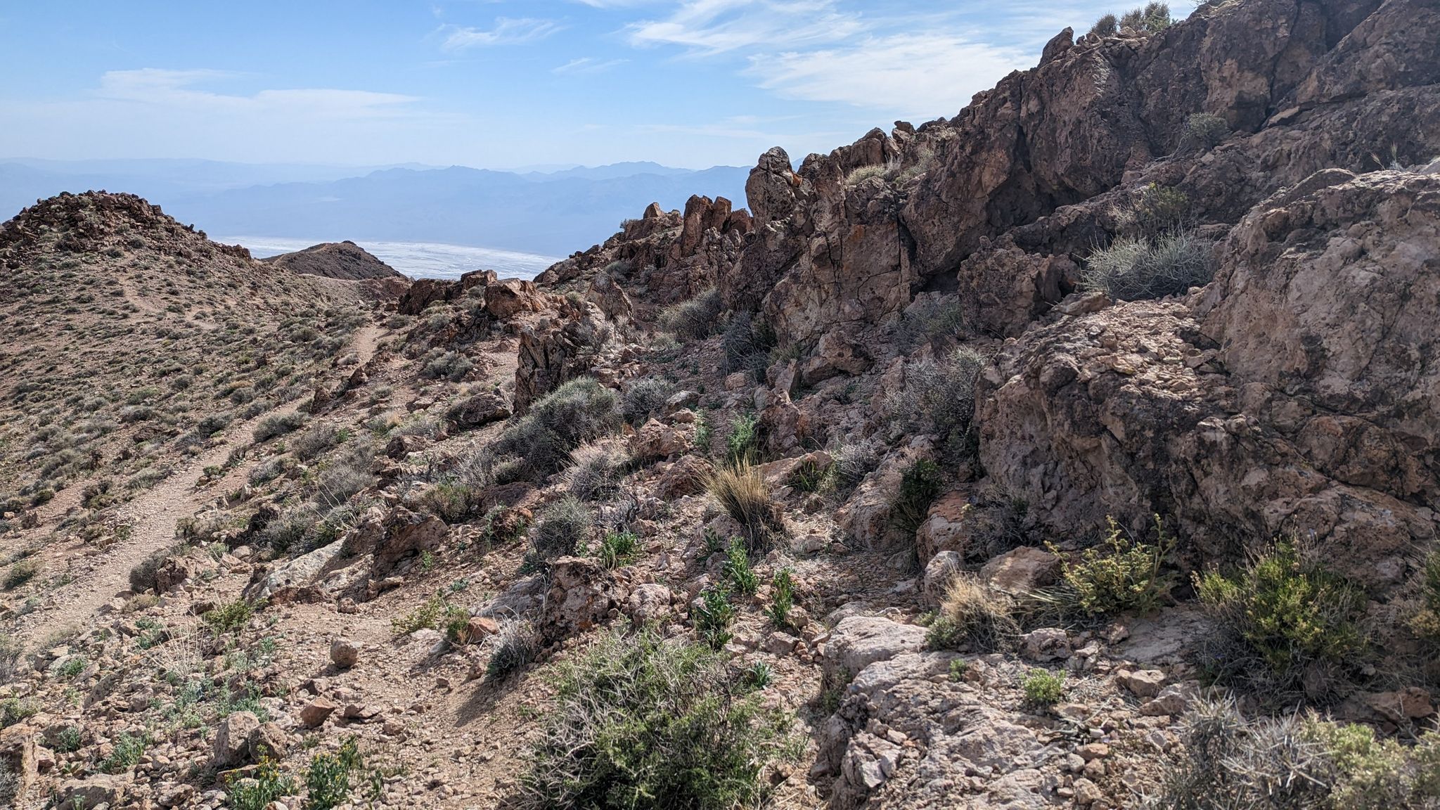 Rocky desert hillside with sparse plants and a distant valley under clear skies. - Dantes Ridge Trail