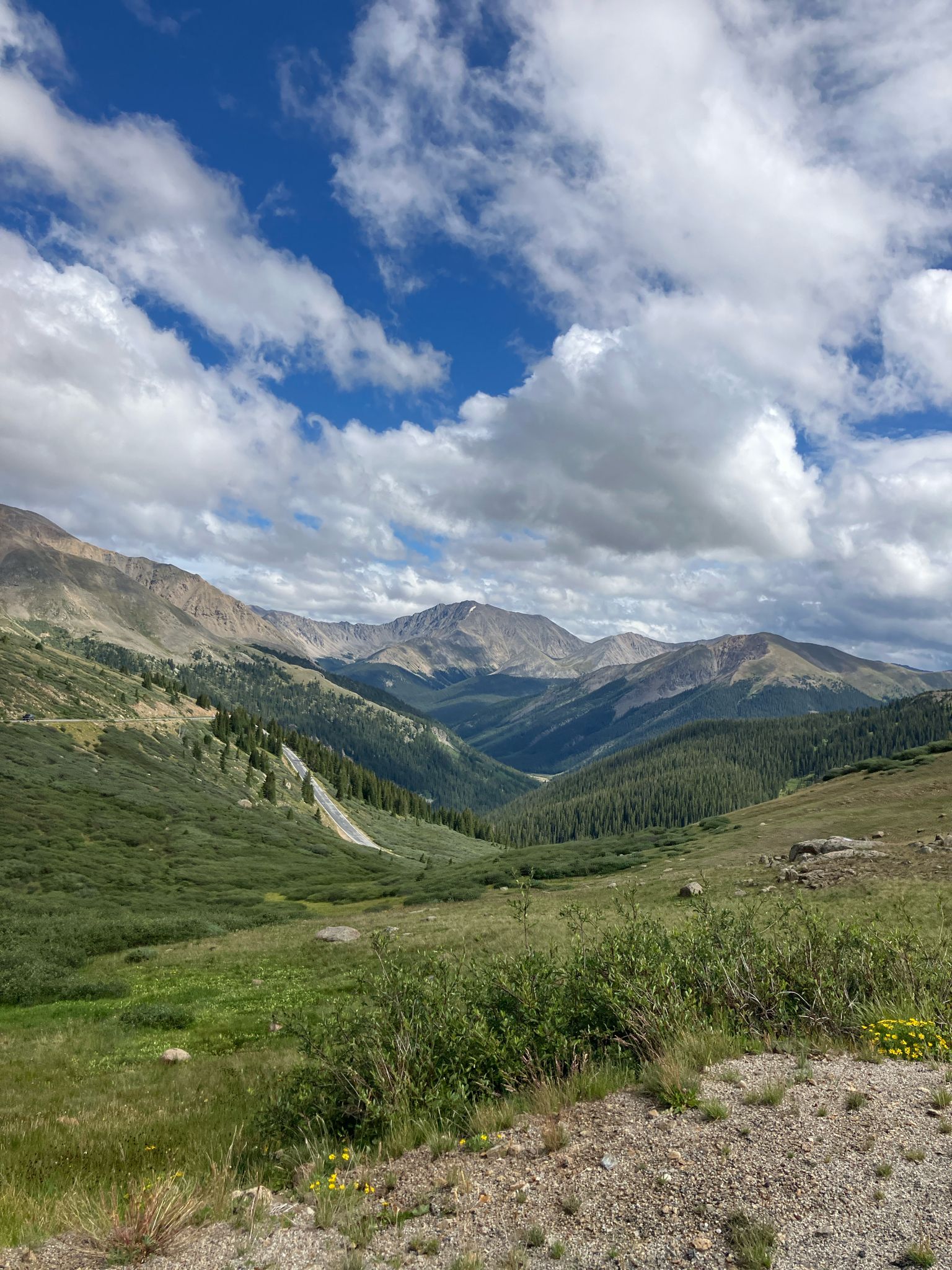 Expansive mountain landscape with green hills, distant peaks, and a cloudy blue sky. - Independence Pass climb from Twin Lakes to Aspen