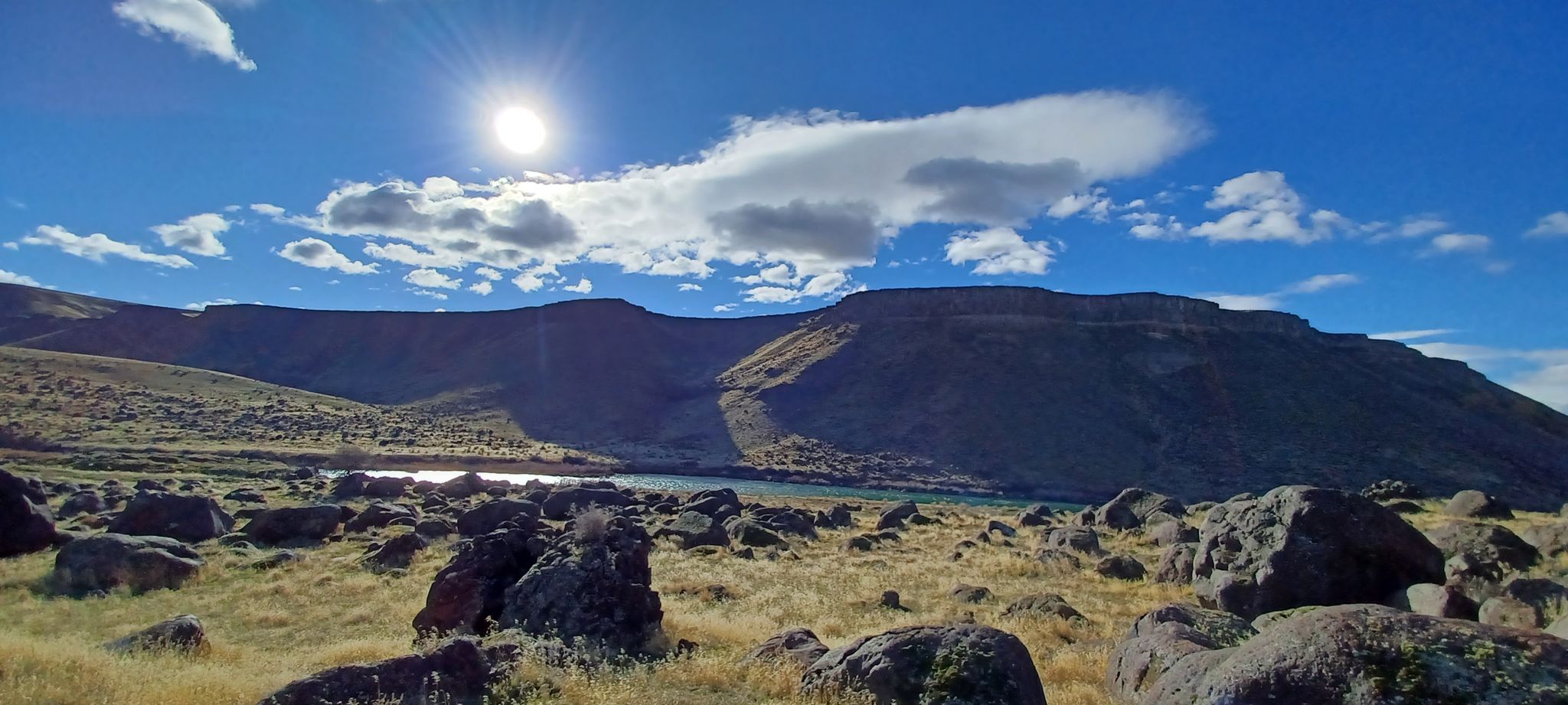 Sunny arid landscape with rocky foreground, large mountains, and a lake. - River Canyon Trail loop