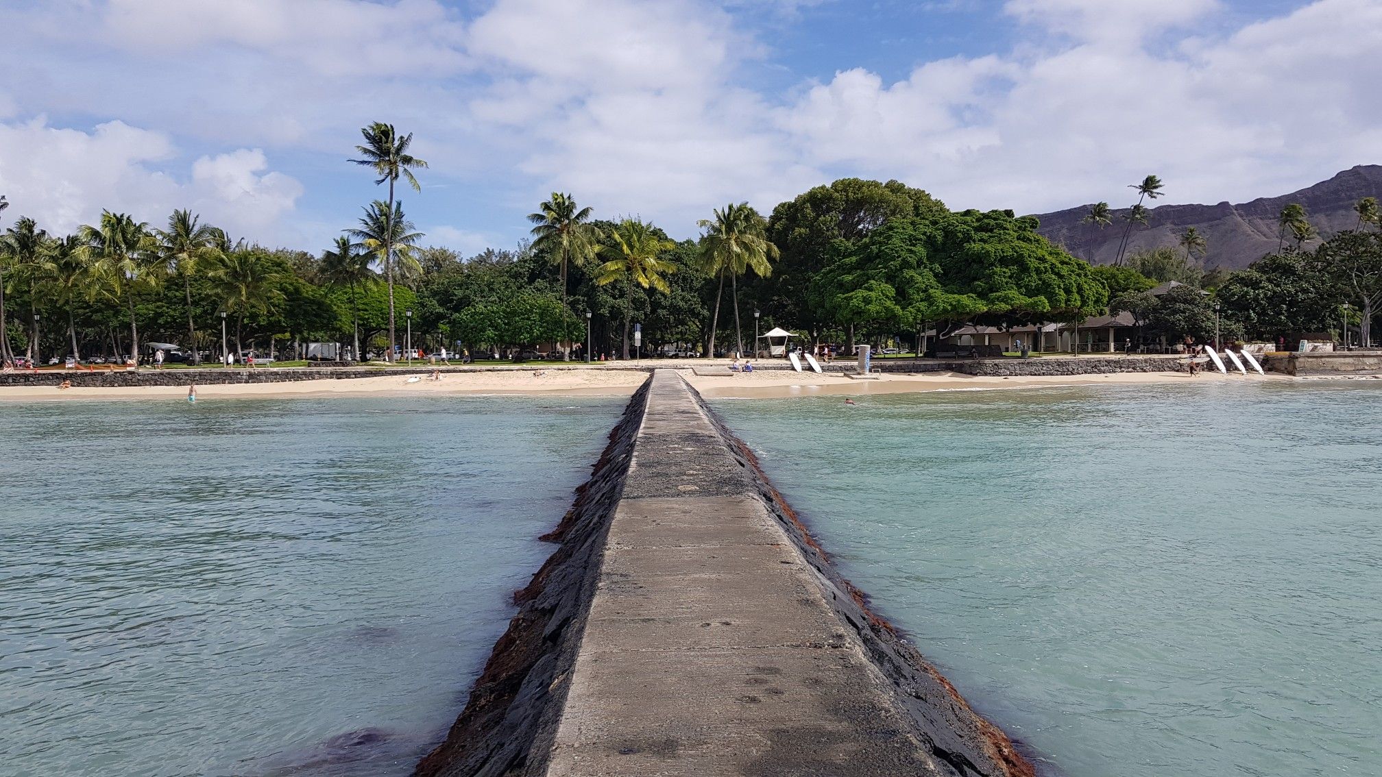 Long concrete pier leading to a sandy beach with palm trees. - Kapiolani Park – Waikiki Beach loop from Waikīkī
