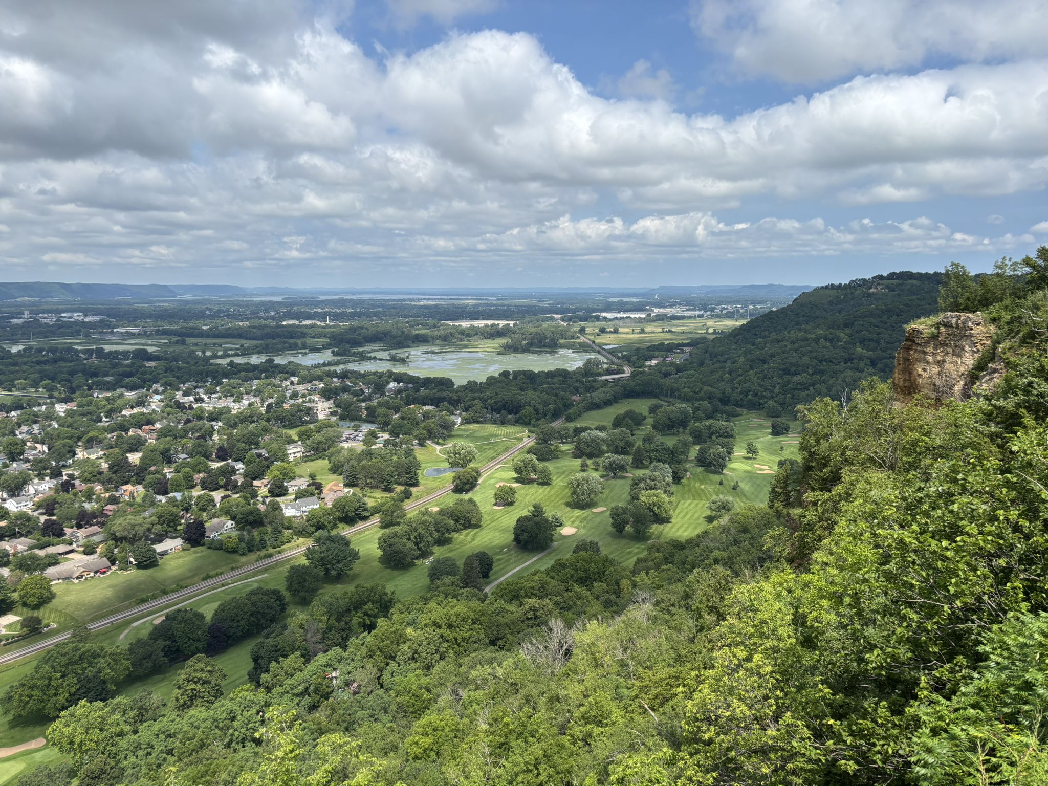 Panoramic view of a town, green golf course, and wetlands under a cloudy sky. - Compass Loop
