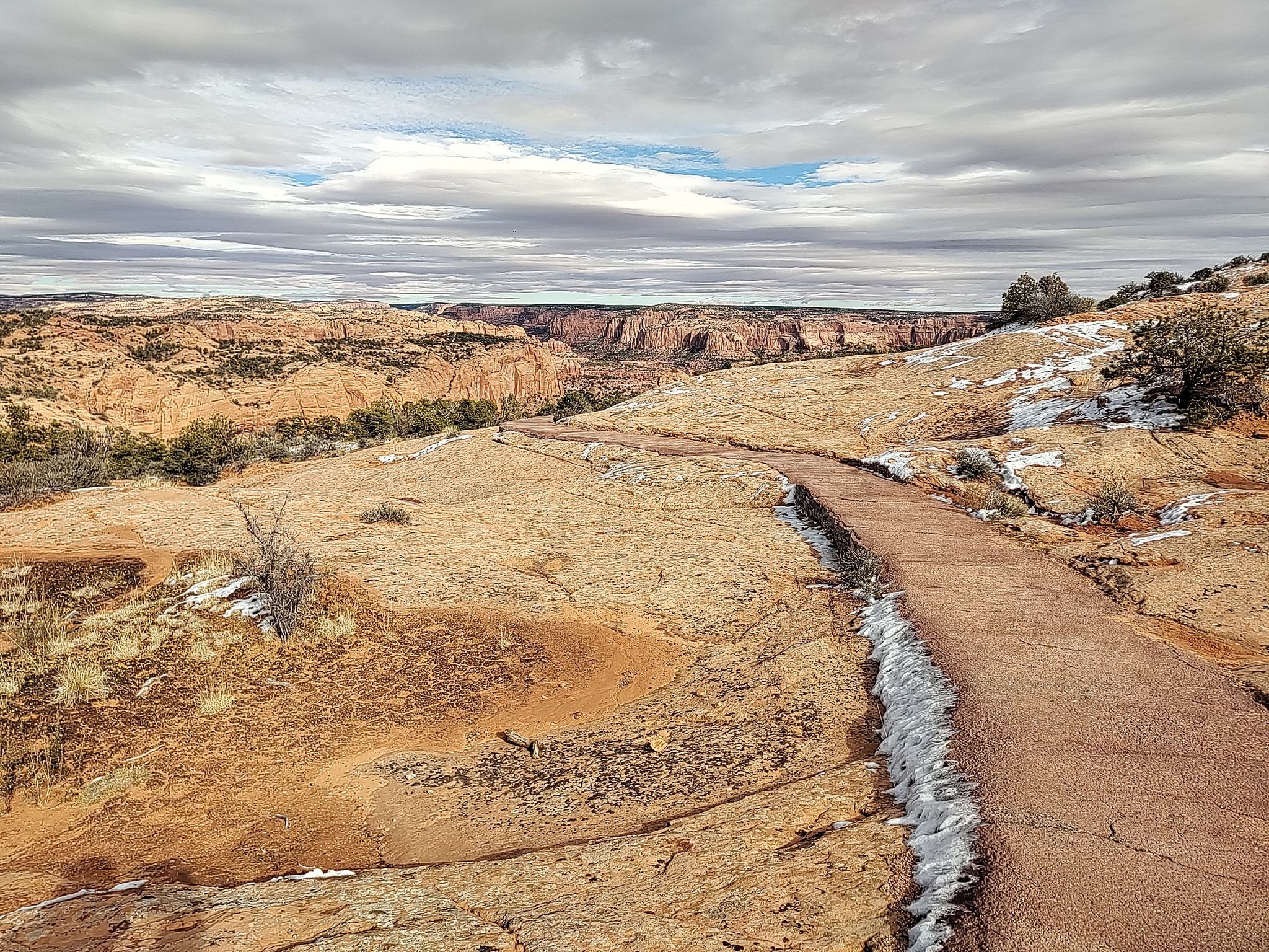 Winding paved path through a snowy desert landscape under a cloudy sky. - Sandal Trail
