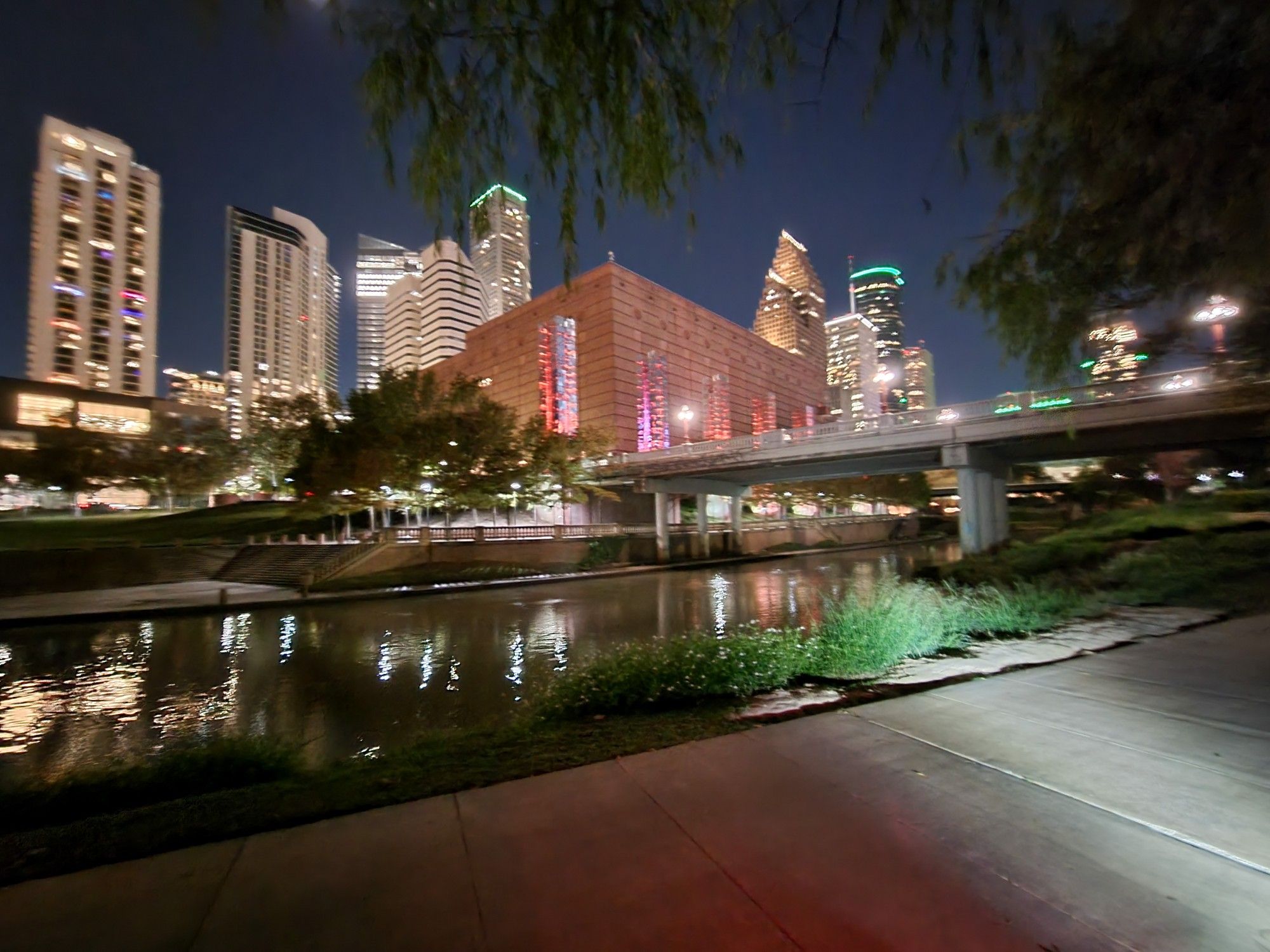 Illuminated city skyline and bridge reflecting on a river at night. - Buffalo Bayou Park Trail