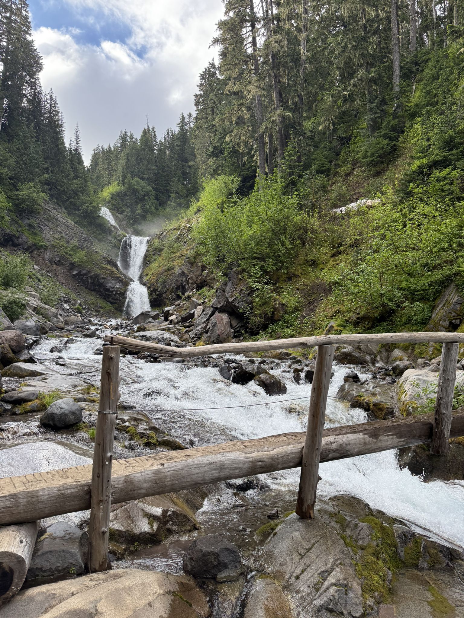 Waterfall and river with a wooden fence in a lush forest. - Comet Falls Trail