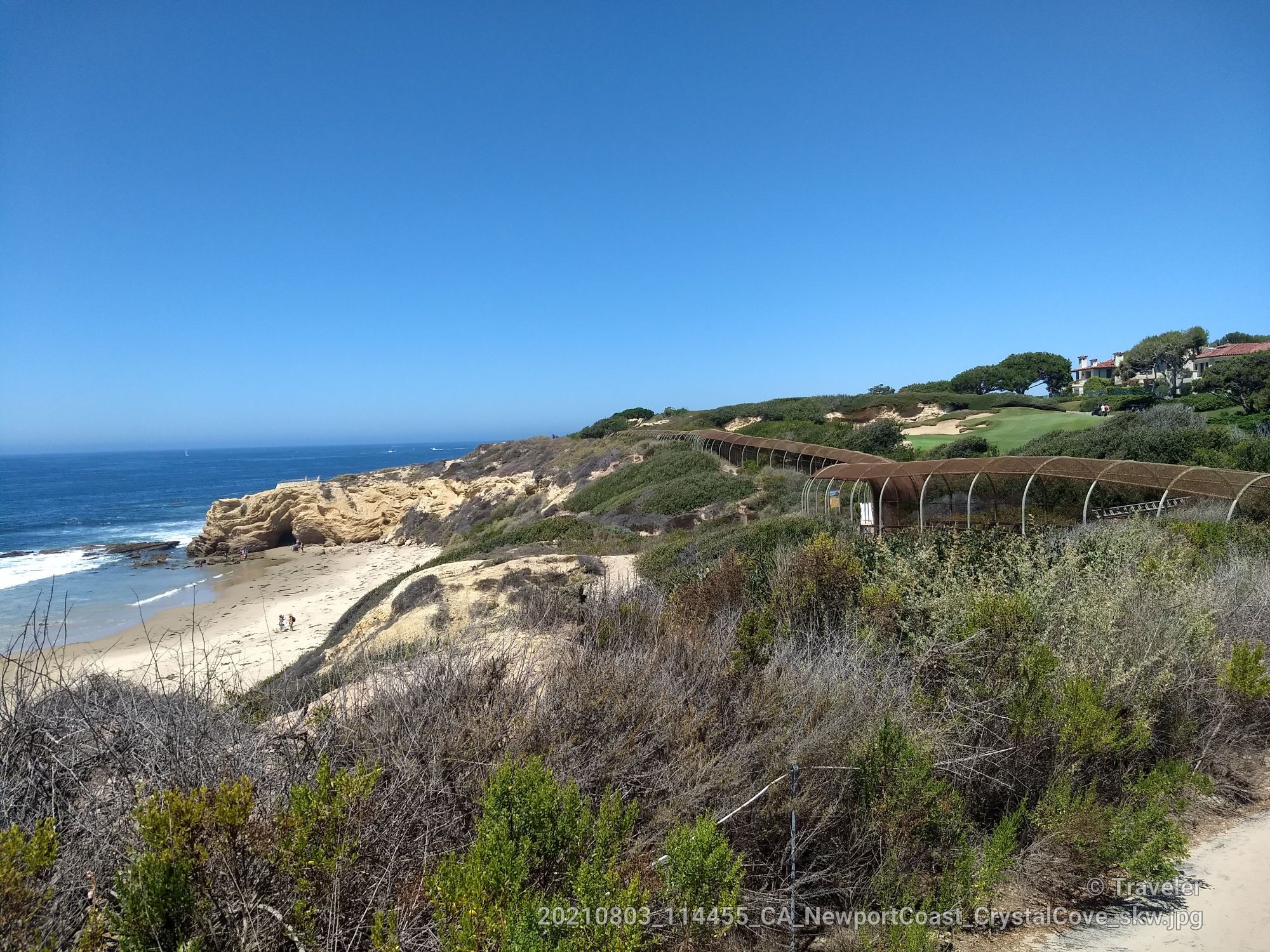 Bright coastal view with sandy beach, blue ocean, rocky cliffs, and hillside structures. - Blufftop Multiuse Trail