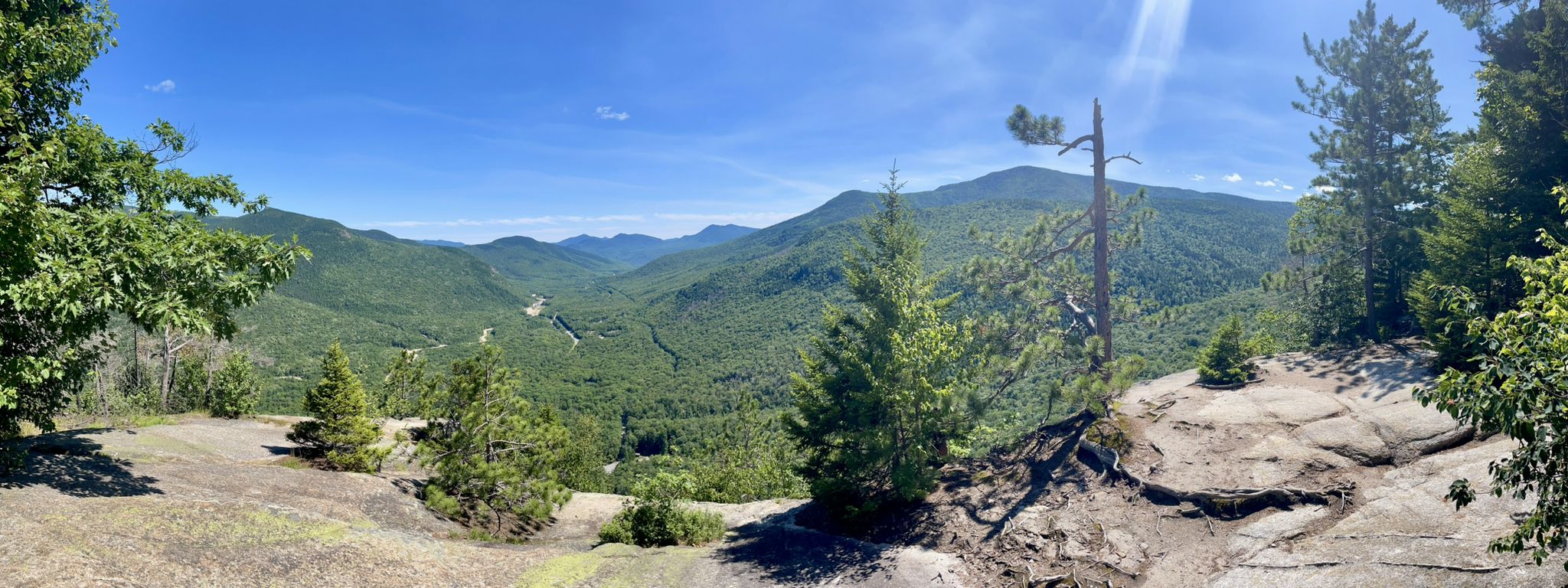 Panoramic view of sunlit green mountains from a rocky overlook. - Ripley Falls and Frankenstein Cliffs Loop