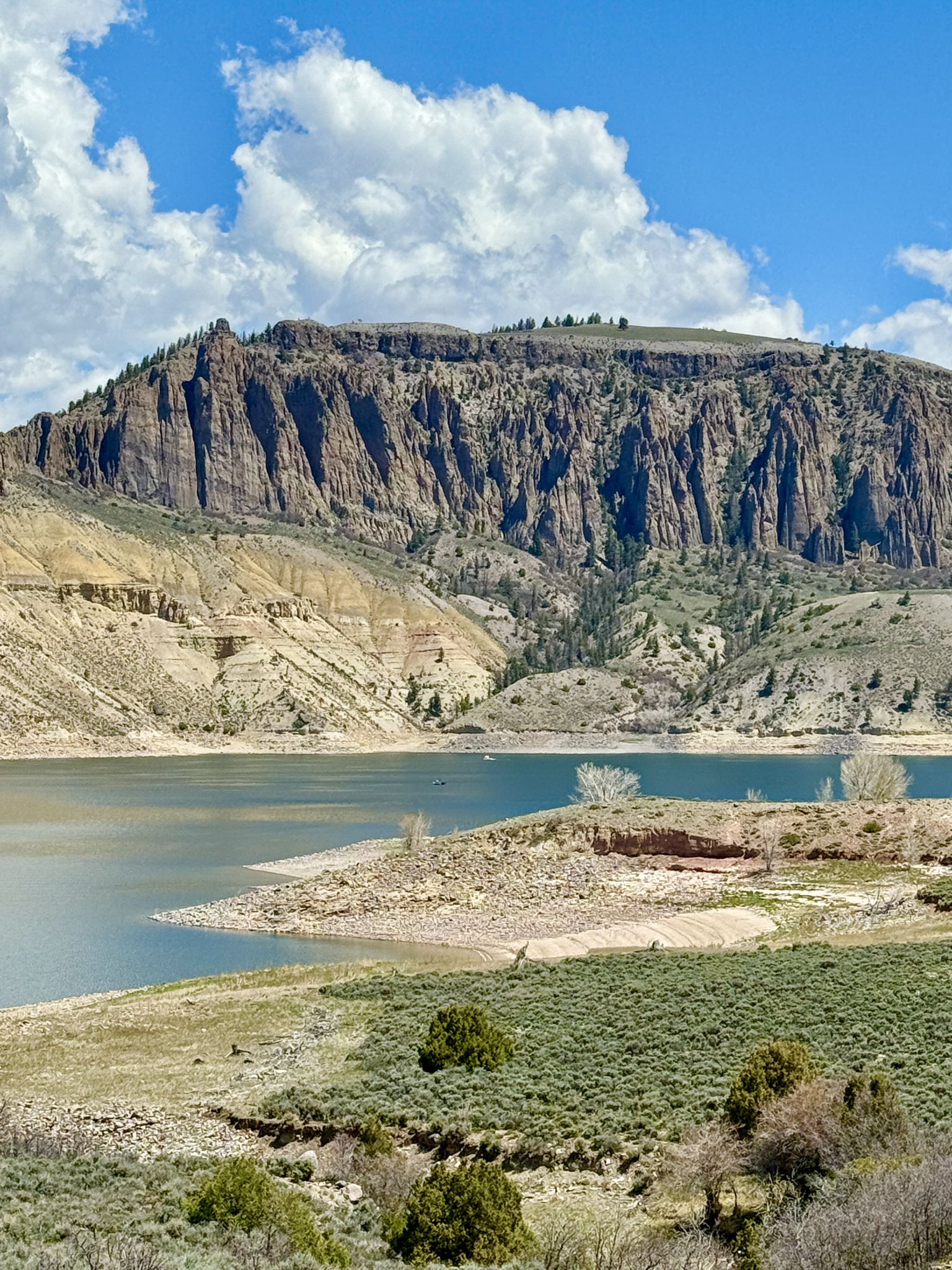 A serene lake with steep rocky mountains under a bright, cloudy sky. - Gunnison to Blue Mesa Dam Overlook