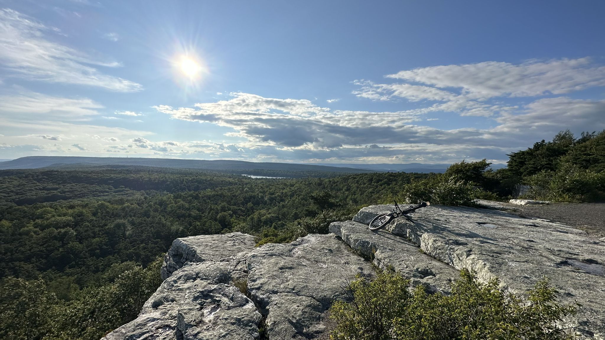 Mountain bike rests on a sunny rocky cliff overlooking a forested valley. - Hamilton Point via Awosting Reserve, Scenic, and Castle Point Road