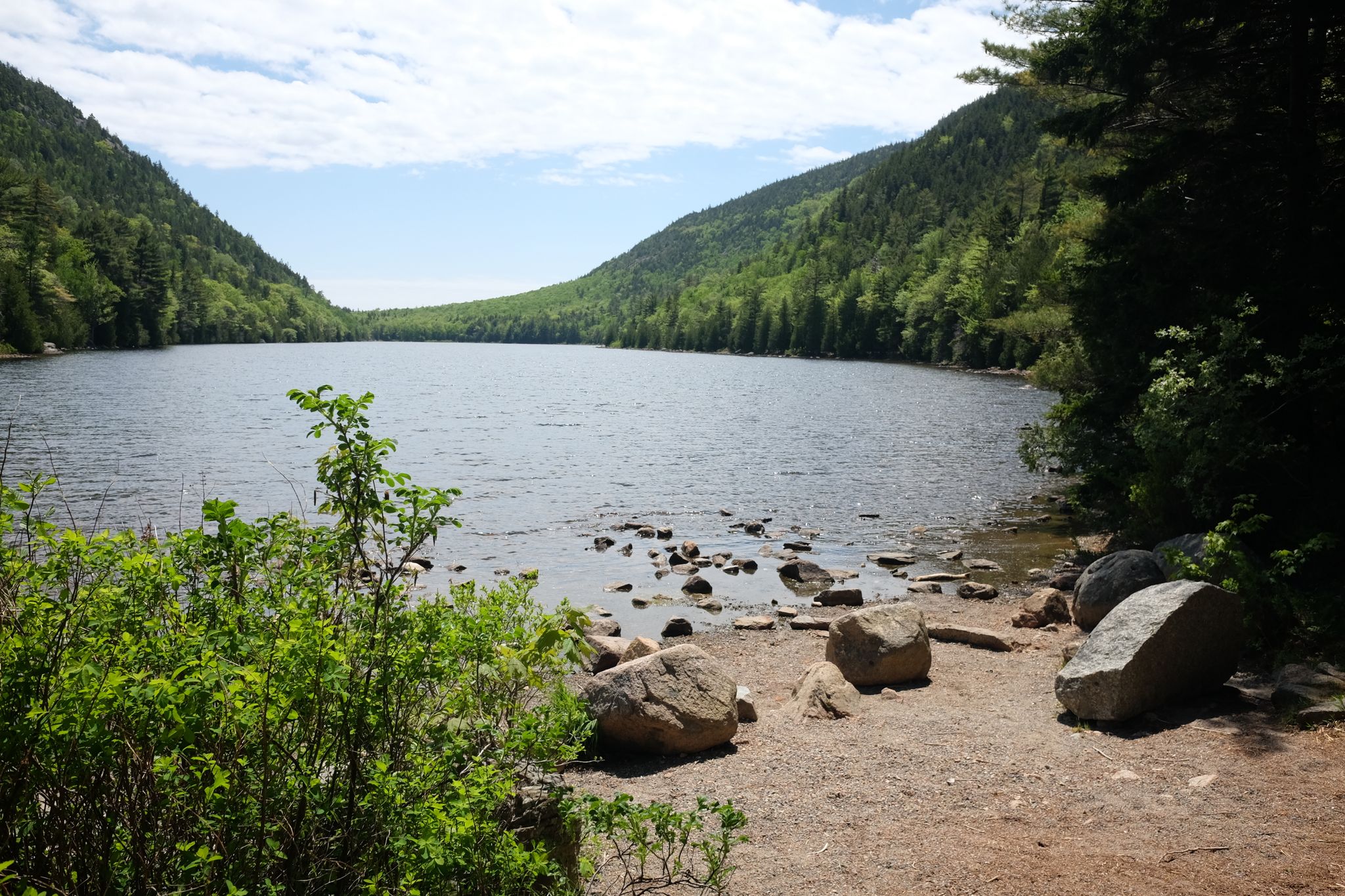 A wide lake surrounded by lush green mountains under a bright sky. - Jordan Pond Gatehouse – Bubble Pond loop from Northeast Harbor