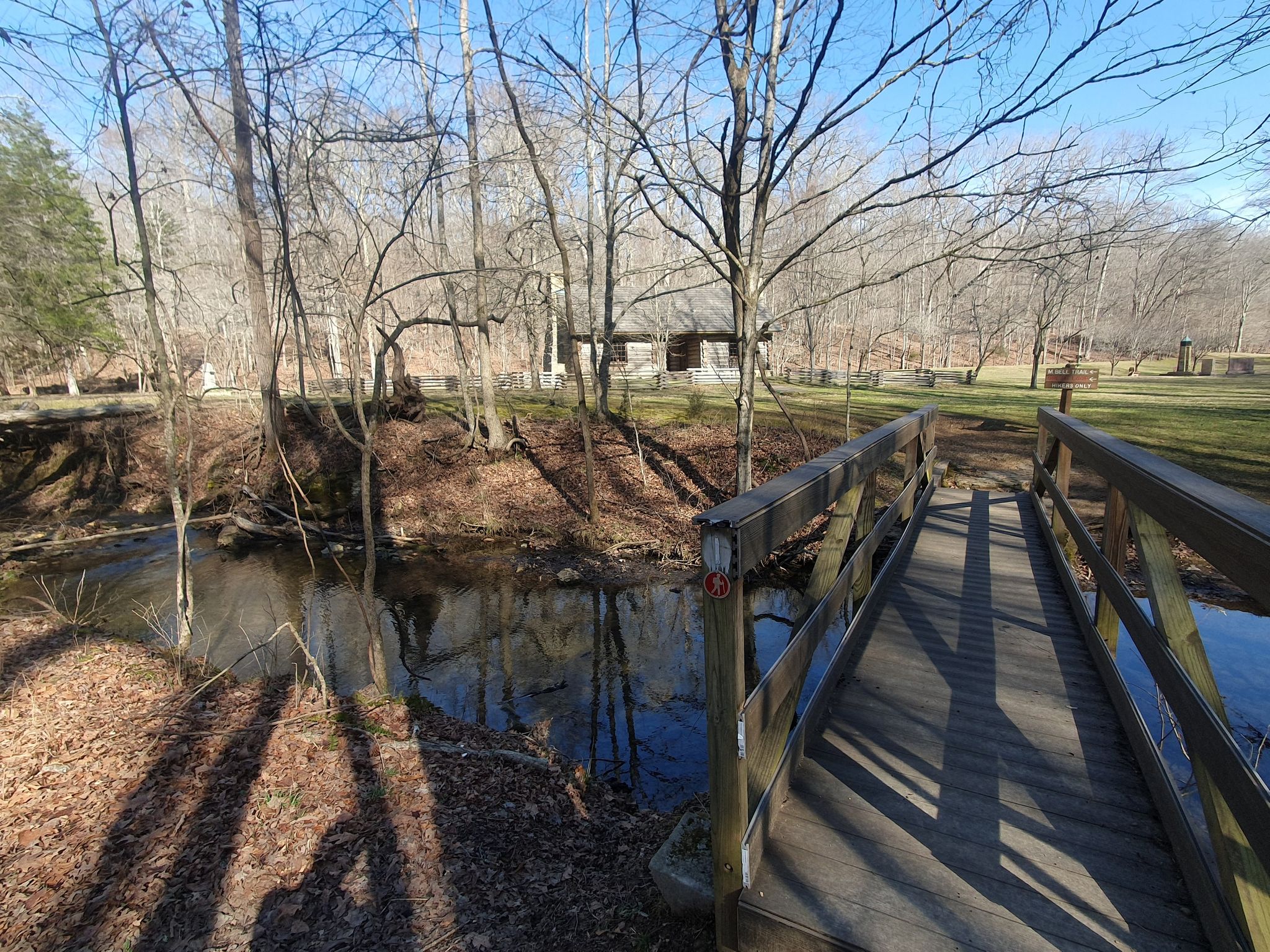 A wooden bridge crosses a small stream in a bare winter forest. - Ore Pit Loop Trail