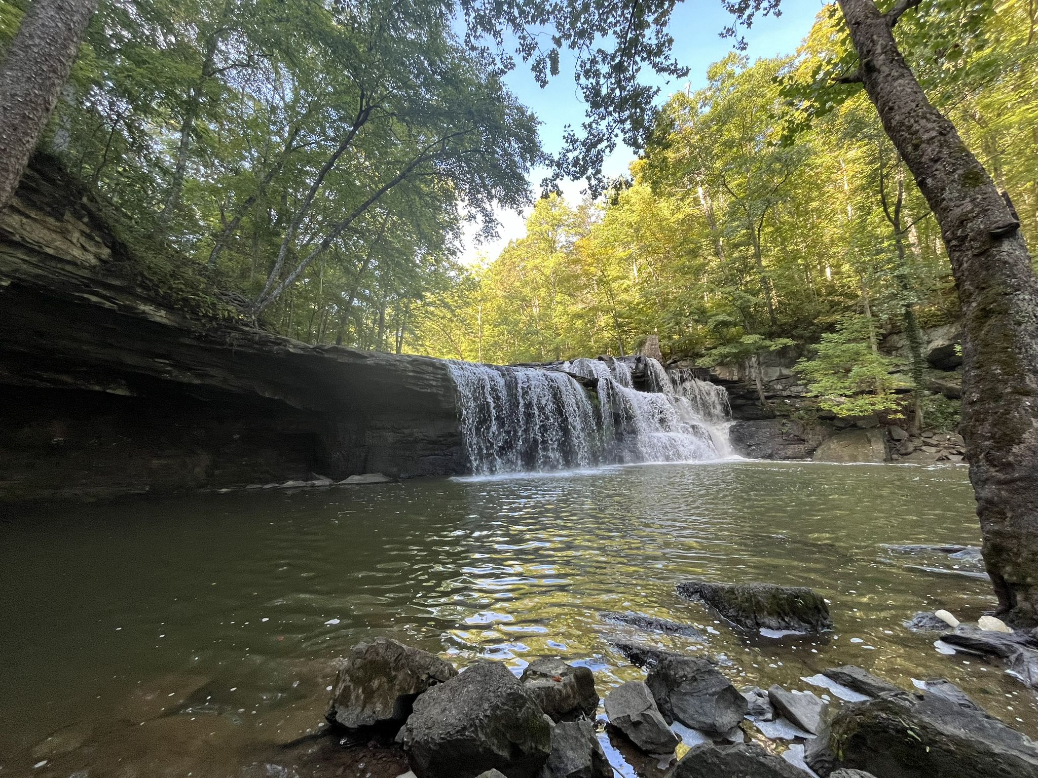 Wide waterfall flows into a calm pool surrounded by lush green forest. - Brush Creek Falls – White Oak Falls loop from Brush Creek Preserve