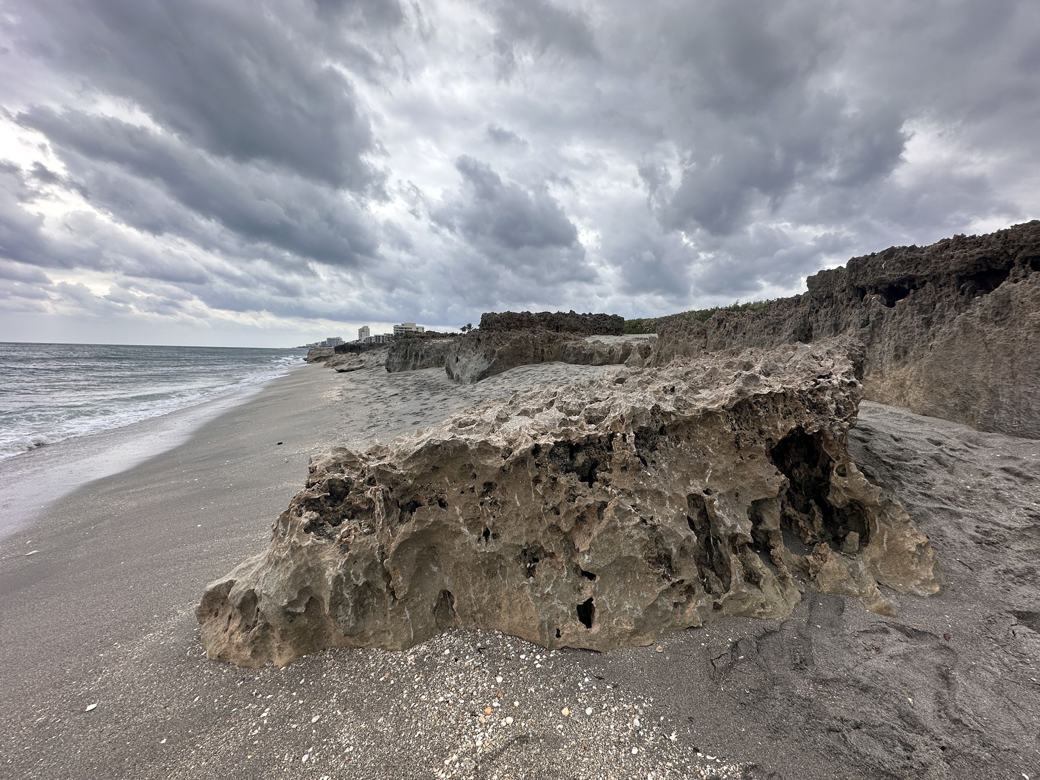 Large eroded rock formation on a dark beach with ocean waves under dramatic clouds. - Blowing Rocks Nature Preserve