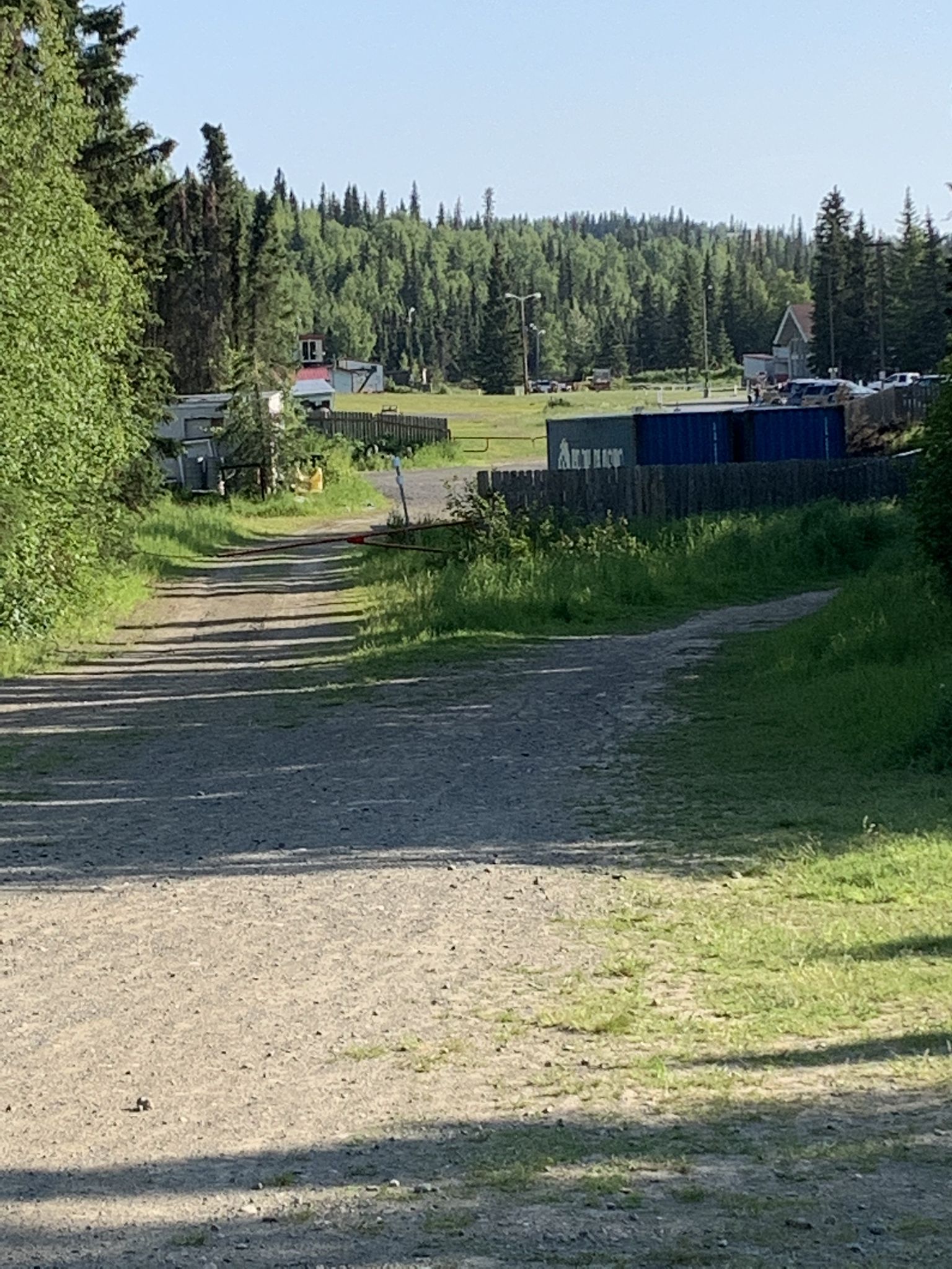 Gravel road leading towards distant buildings and containers in a sunny forest. - Abbott Multi-Use Trail – Tour of Anchorage Trail loop from Sahalee Homeowner's Association