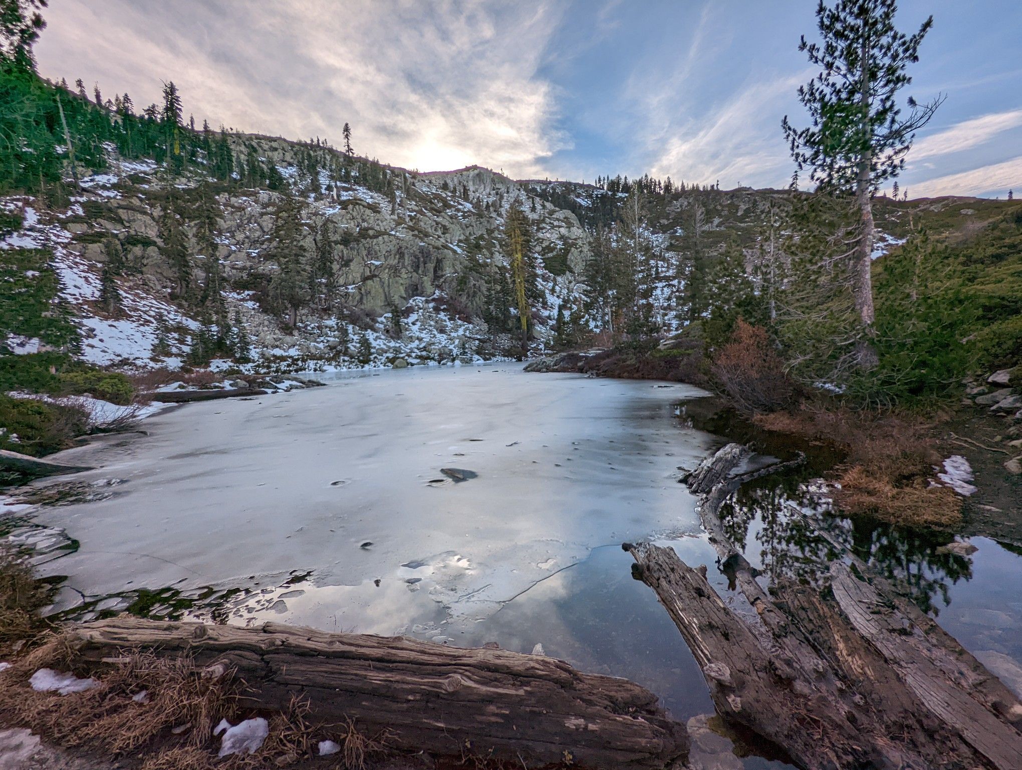Iced-over lake surrounded by snowy, rocky mountains and evergreen trees under a cloudy sky. - Heart Lake Trail