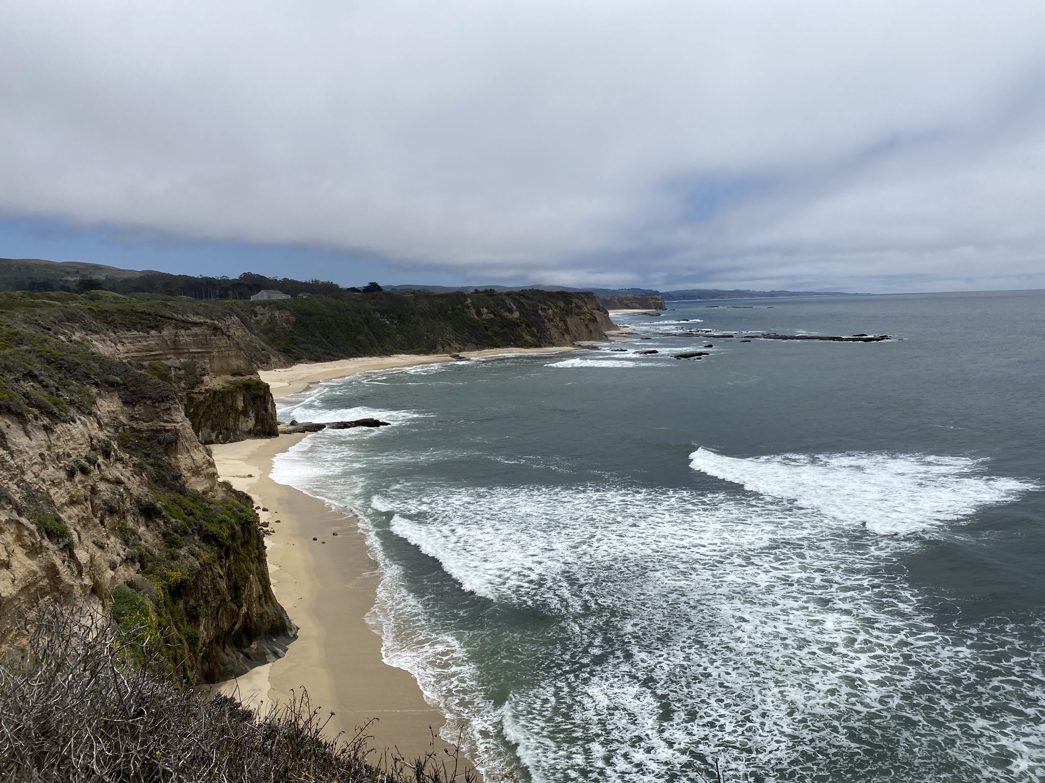 Wide view of a sandy beach and ocean waves crashing against cliffs. - Cowell-Purisima Trail