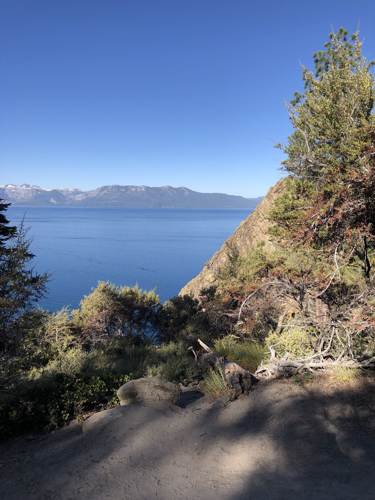 Clear day overlooking a blue lake with distant snow-capped mountains and green trees. - Cave Rock Overlook