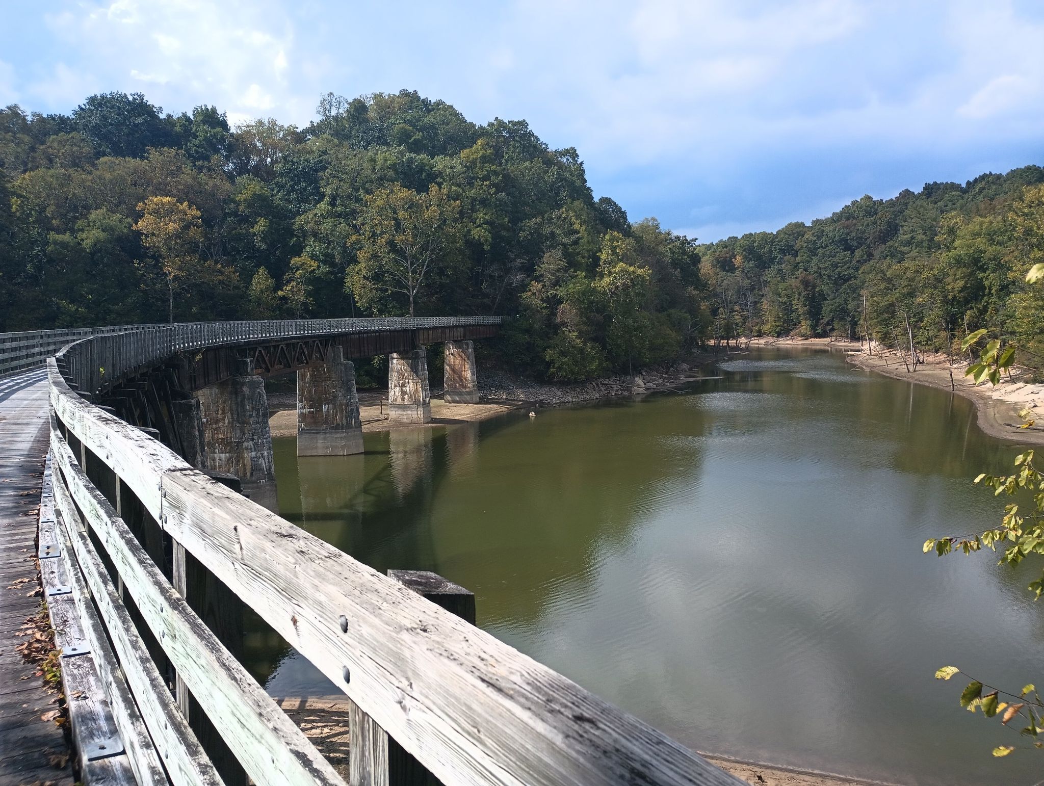 A curved wooden bridge extends over a river, surrounded by forested hills. - Damascus City Park – Holston River Confluence loop from Damascus