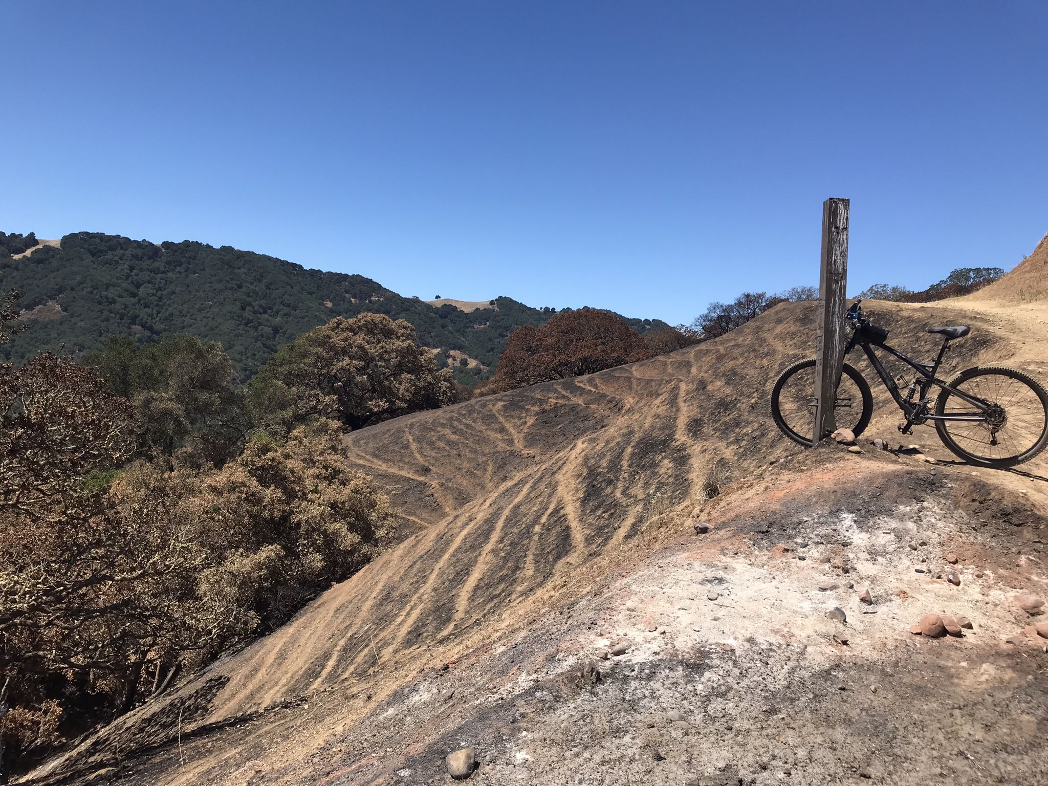 Mountain bike leaning on a post on a dry, sunny hillside with green mountains. - Valley View Trail to Blue Oak Trail Loop