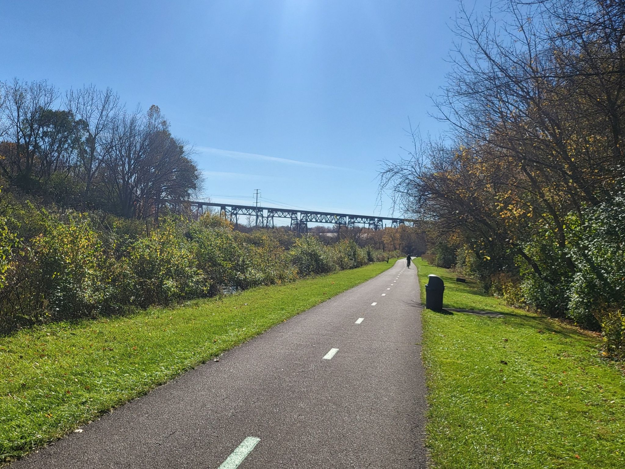A paved path stretches towards a distant bridge under a bright, sunny sky. - Ohio & Erie Canal Towpath Trail