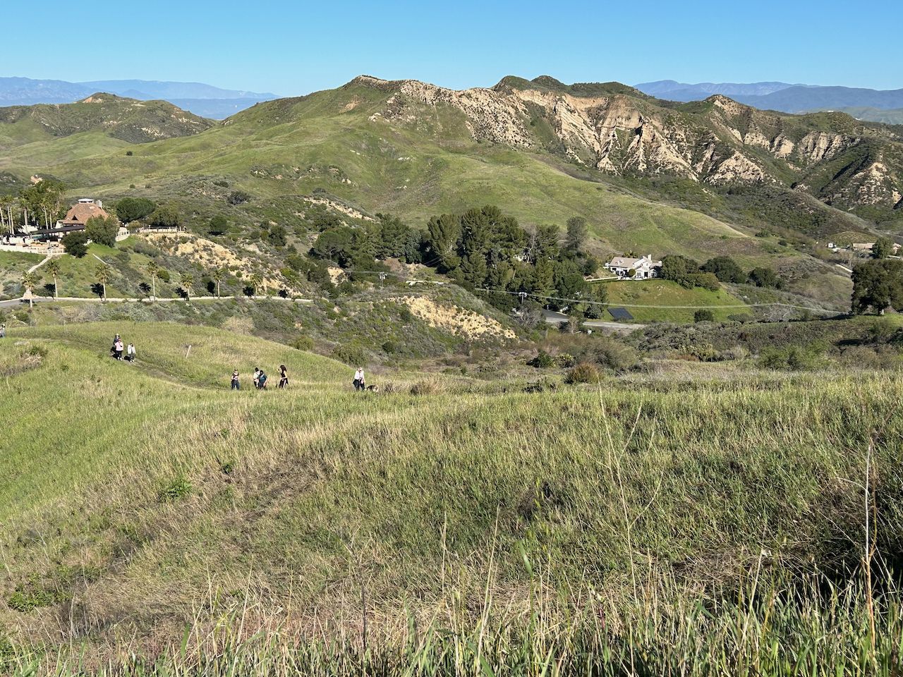Group of people hiking on a grassy hillside with distant mountains. - East Walker Loop