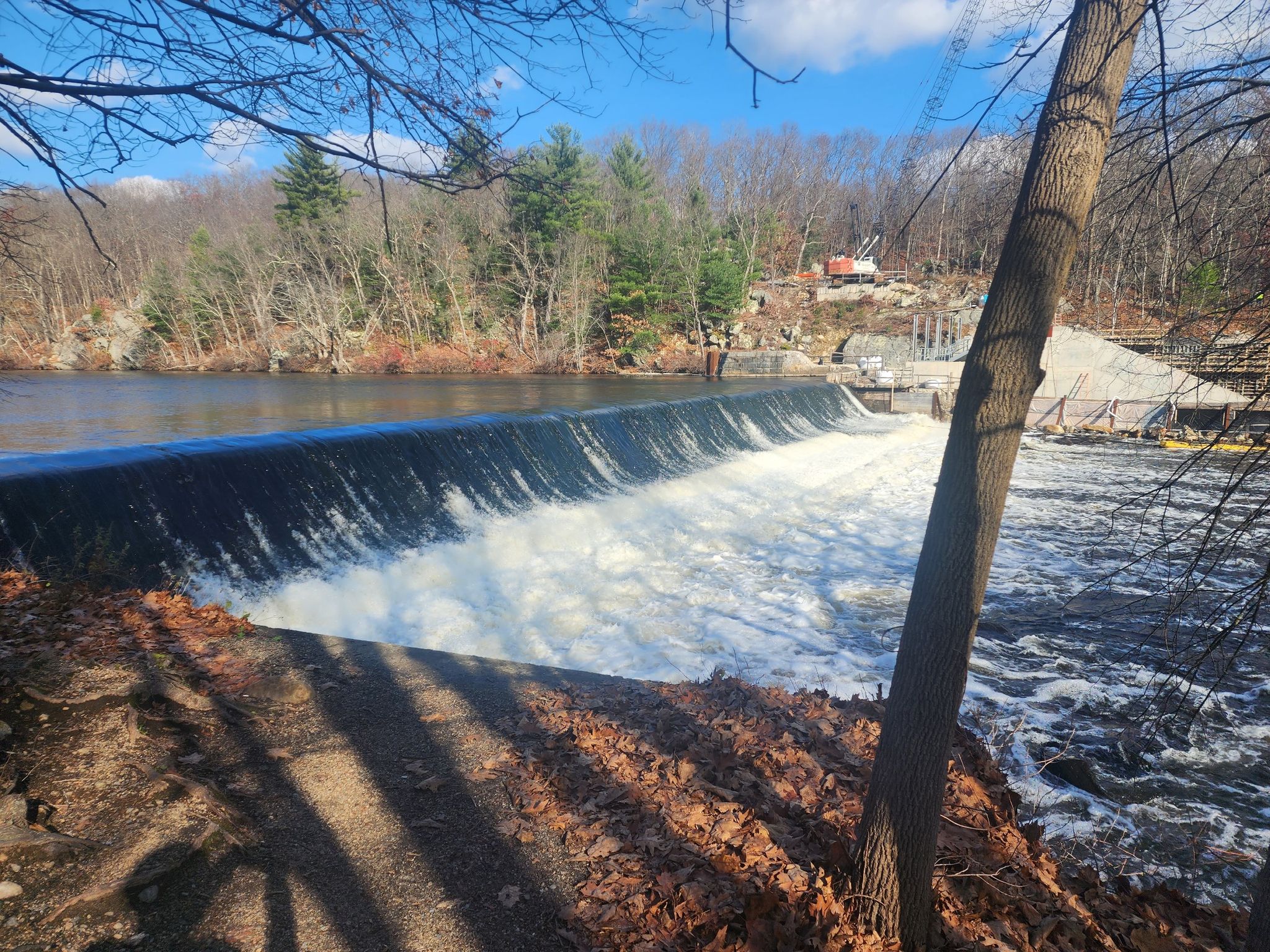 A wide waterfall cascades over a dam under a bright blue sky. - Along the Blackstone River – Blackstone River Bikeway loop from Albion