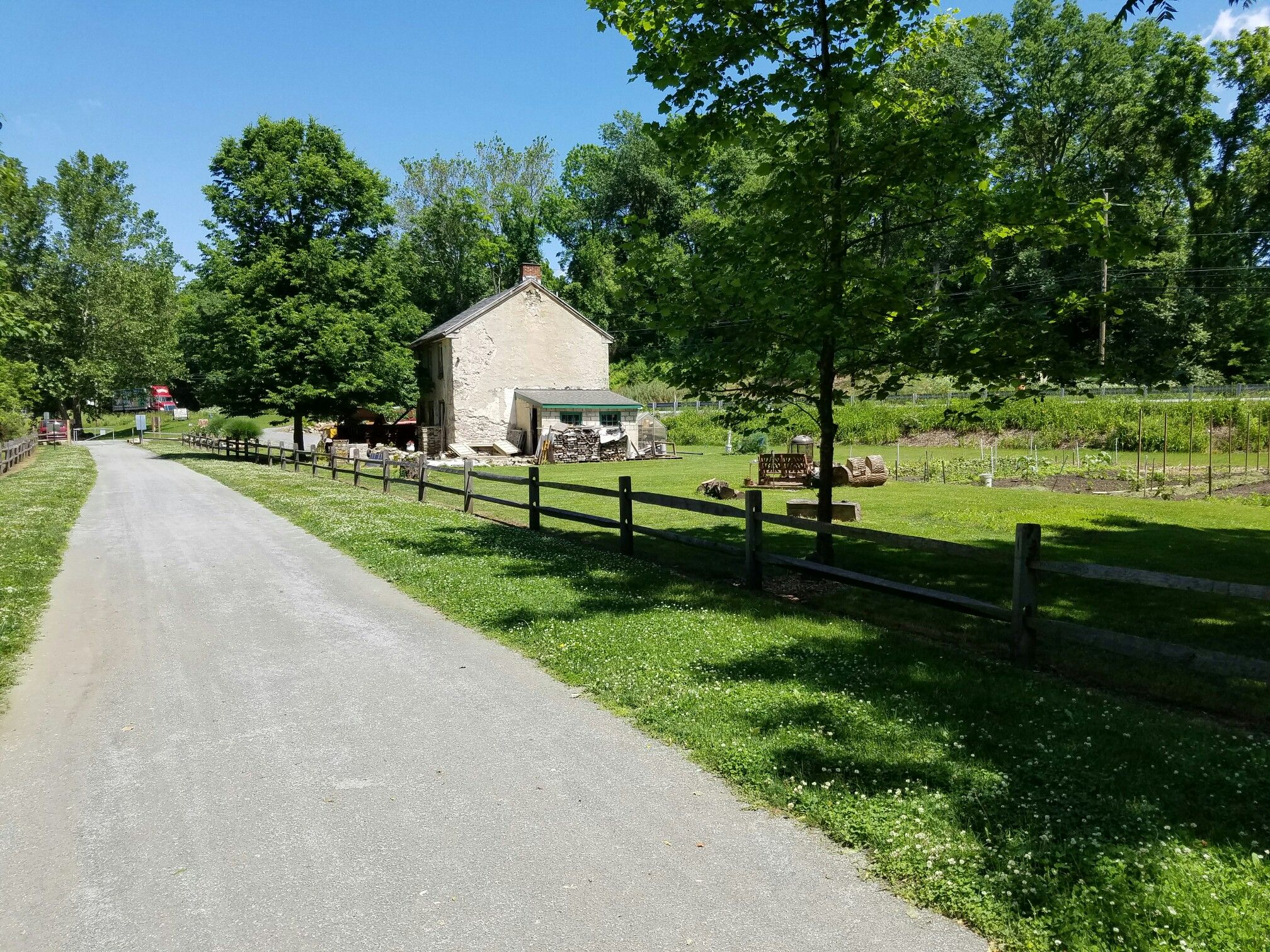 Gravel path next to wooden fence, old stone building, green fields. - Old Trolley Line Bridge loop from Marietta