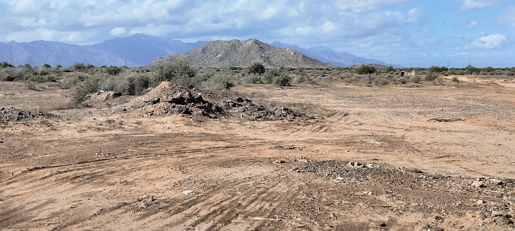 Arid desert landscape with rocky mounds, sparse brush, and distant mountains under clouds. - Sacaton and Casa Grande loop from Maricopa