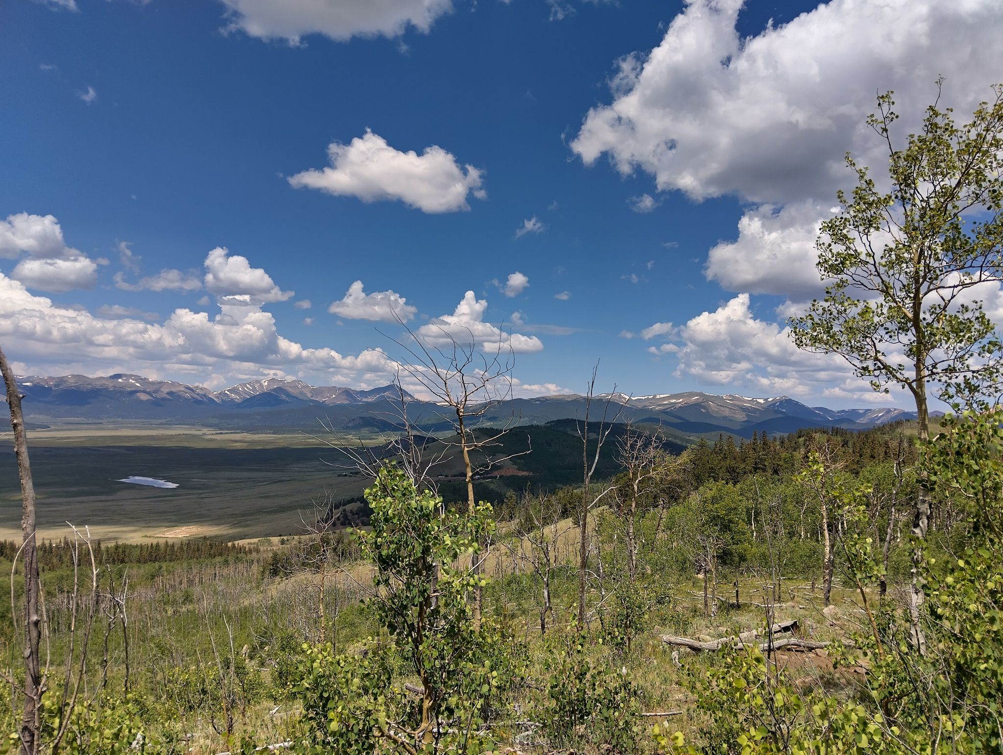 A scenic view of a green valley and snow-capped mountains under a cloudy sky. - Kenosha Pass Campground – Kenosha Pass loop from Kenosha Pass Overlook