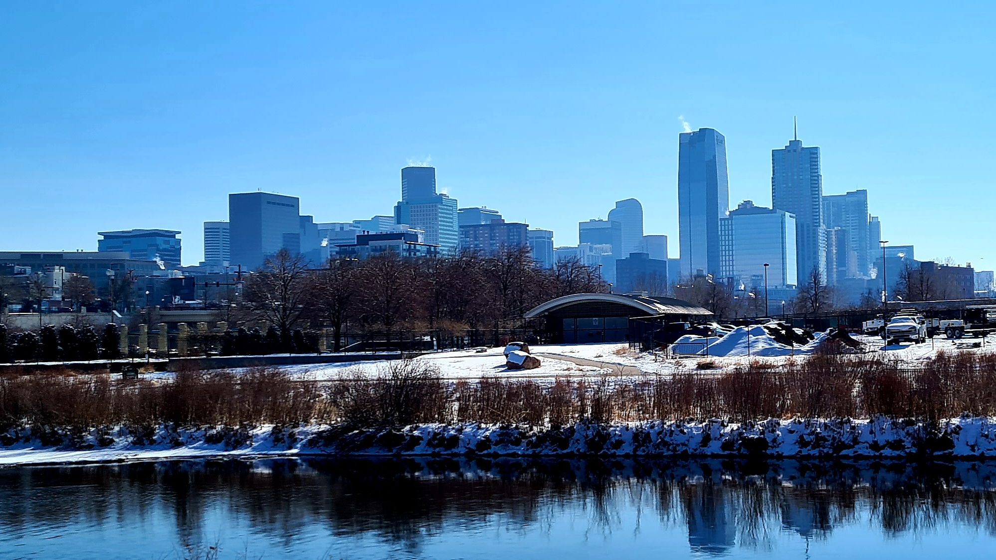 City skyline across a snowy river, reflecting under a clear blue sky. - Mile High Stadium and Cherry Creek Trail