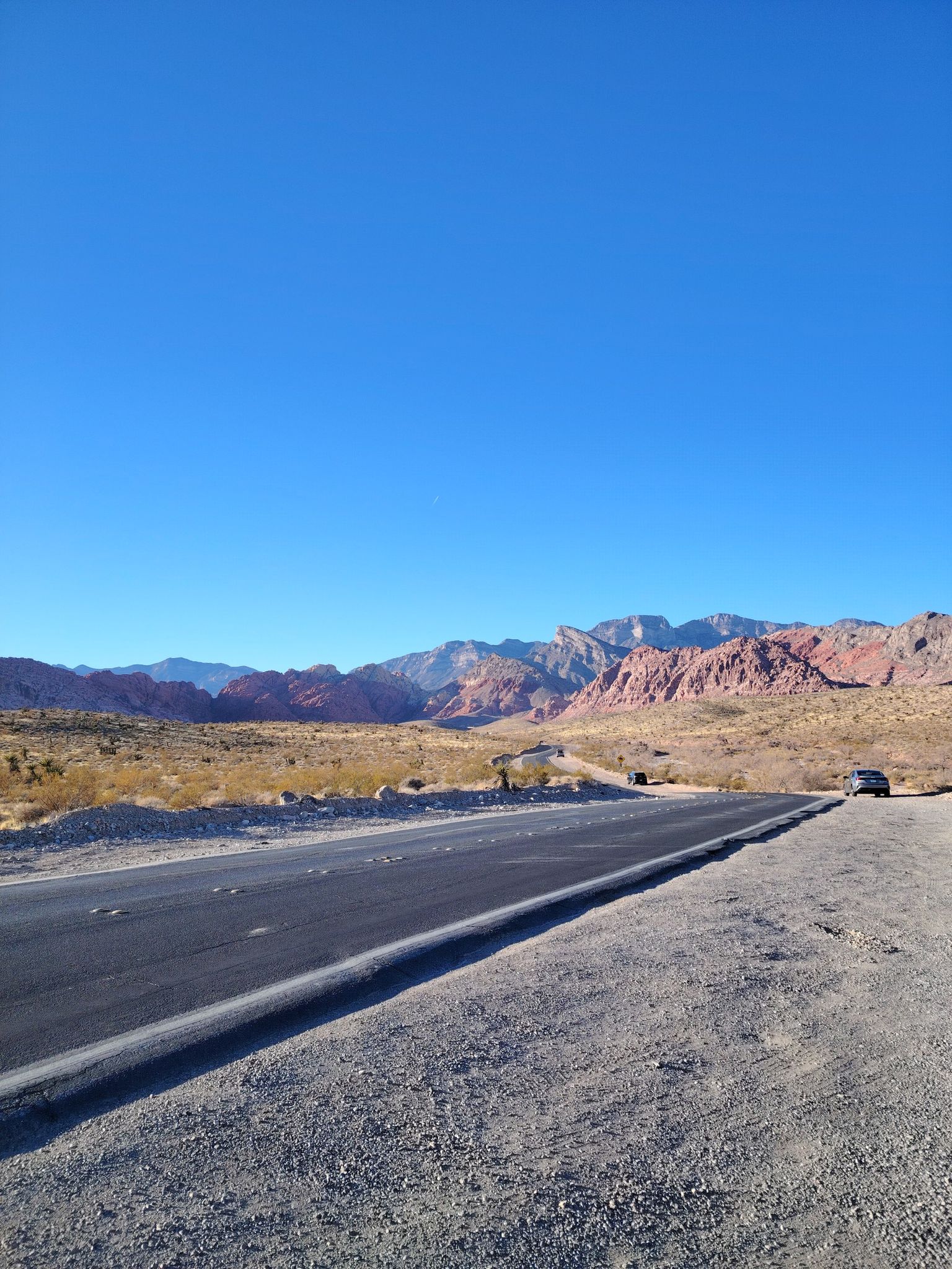 Long road through a sunny desert landscape with distant red rock mountains. - Northern Beltway Trail – Downtown Summerlin loop from Centennial Hills