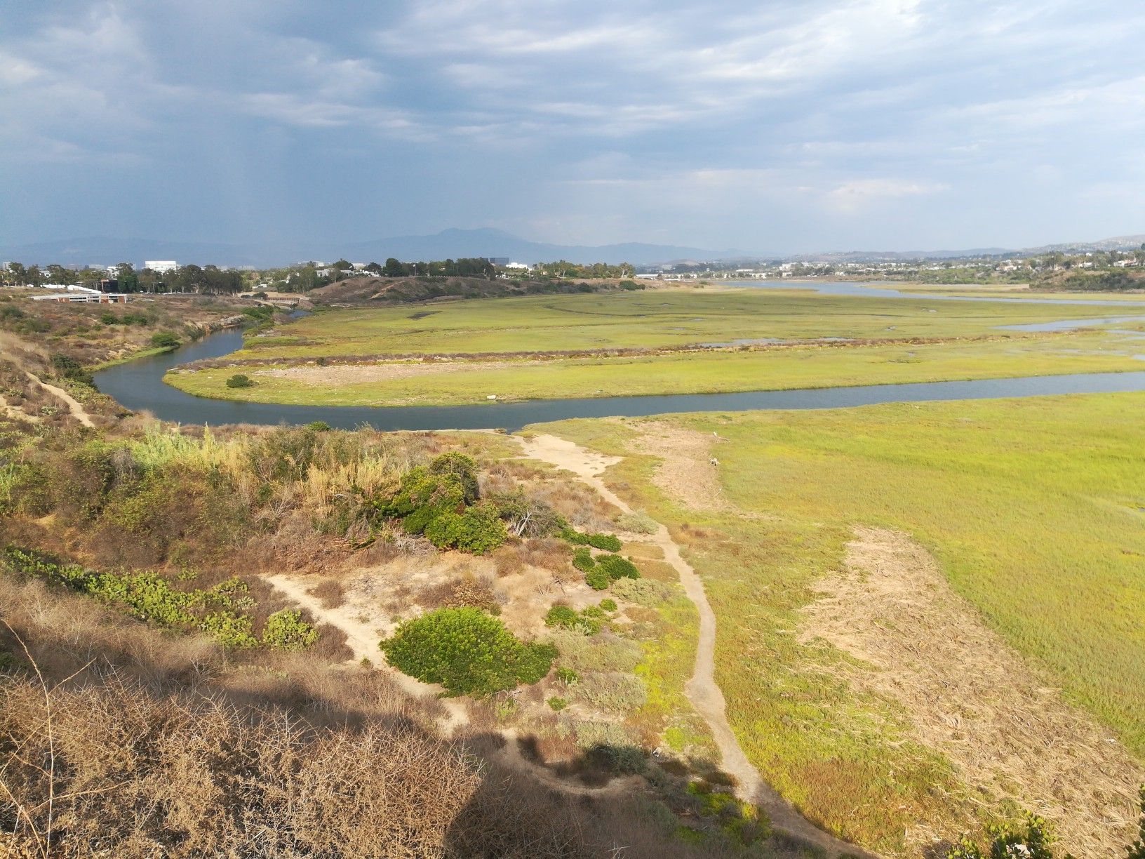Aerial view of a winding river through green and dry fields under a cloudy sky. - Back Bay Loop Trail
