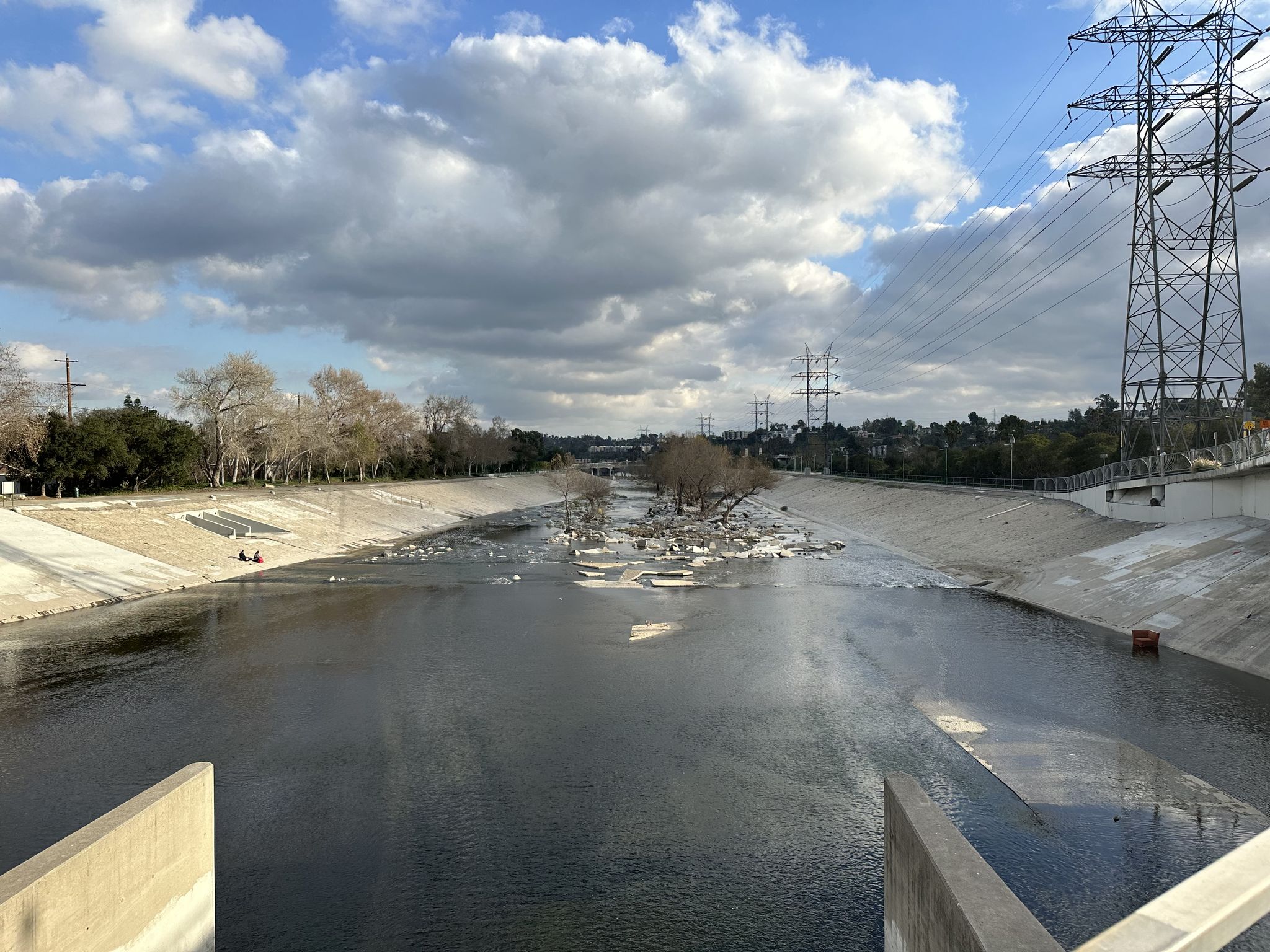 Wide concrete river channel under cloudy sky with power lines overhead. - Flint Peak Loop