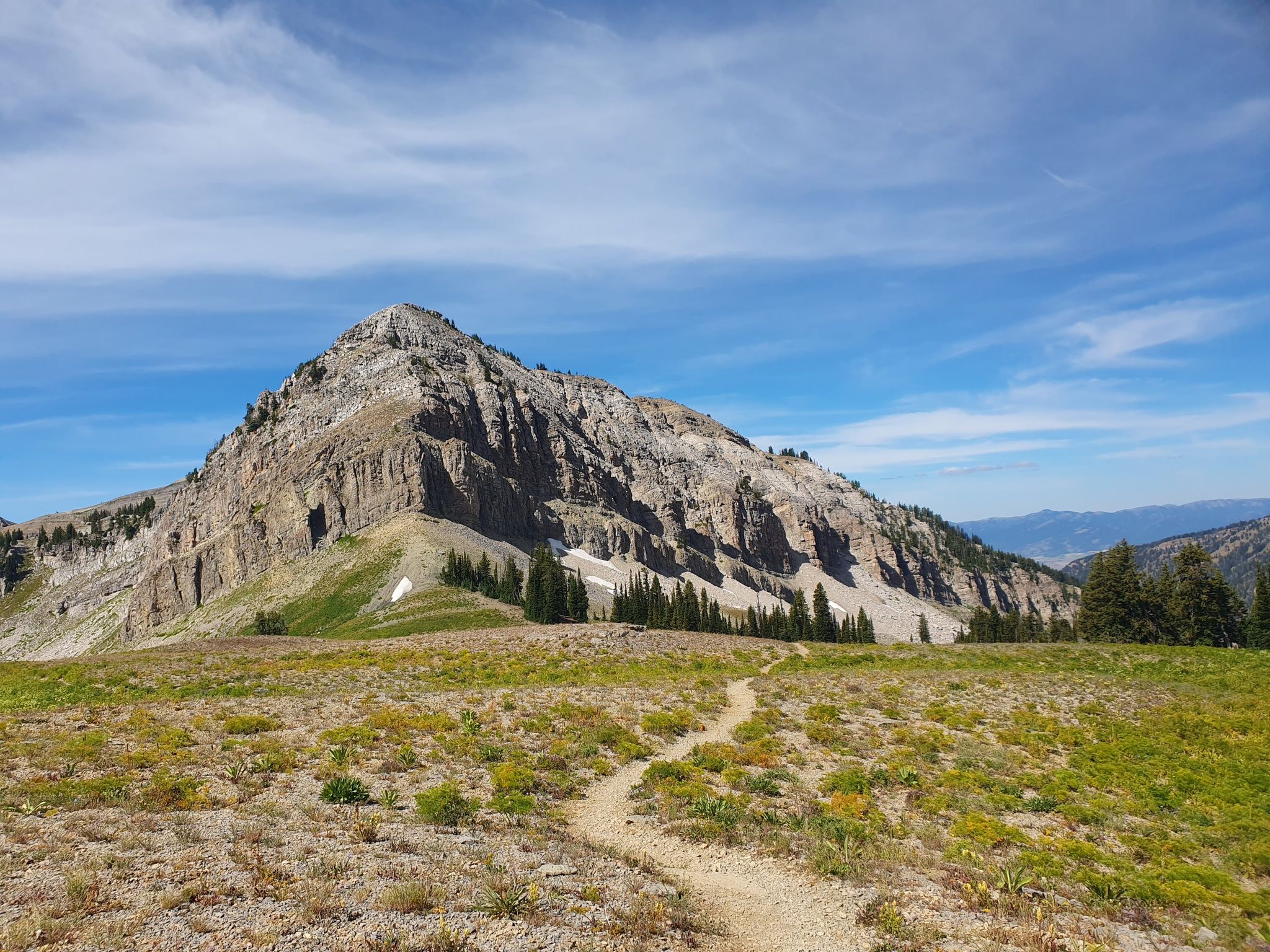 A dirt trail leads towards a large rocky mountain under a bright sky. - Teton Crest Trail: Granite Canyon to Jenny Lake