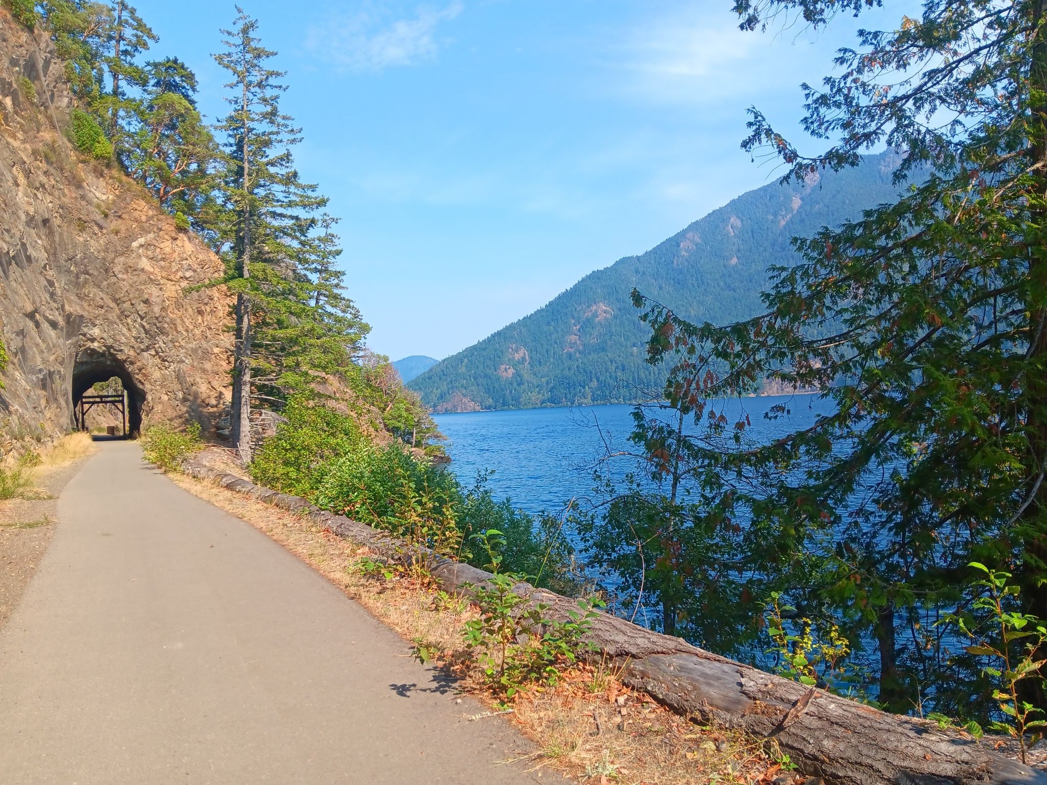 Paved path leading to a tunnel through a rock face, beside a large lake. - Lake Crescent – Daley Rankin Tunnel loop from Fairholm