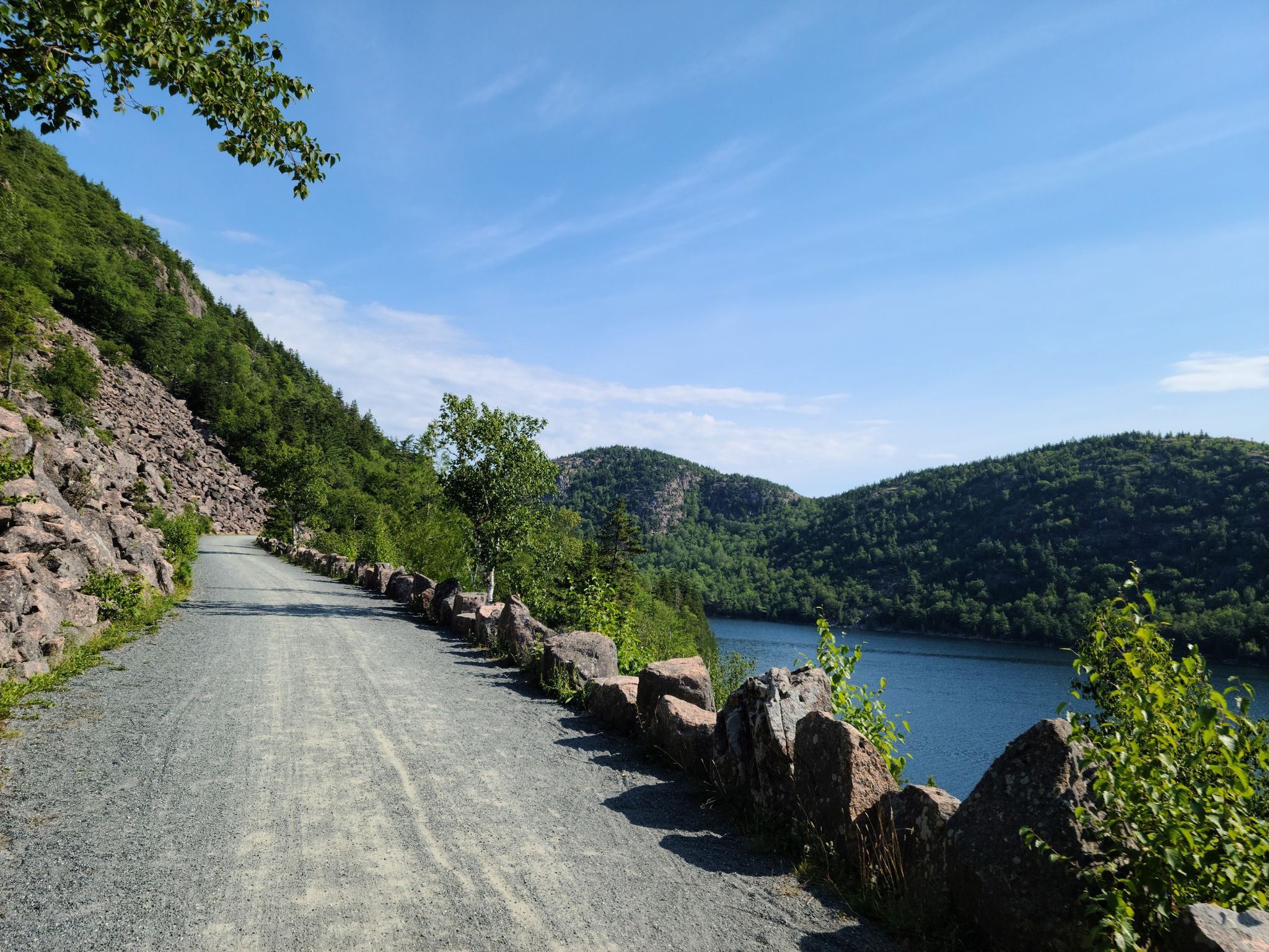 Gravel path with stone wall overlooking a lake and forested mountains. - Tri Lakes Loop