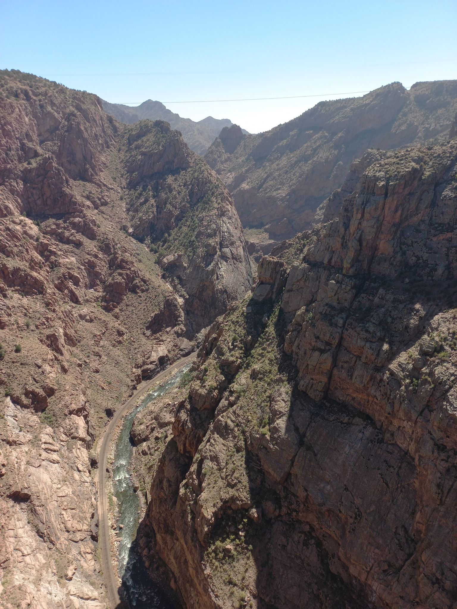 Deep, rocky canyon with a river and train tracks under bright sunlight. - Viewpoint – Royal Gorge Bridge loop from Royal Gorge Bridge