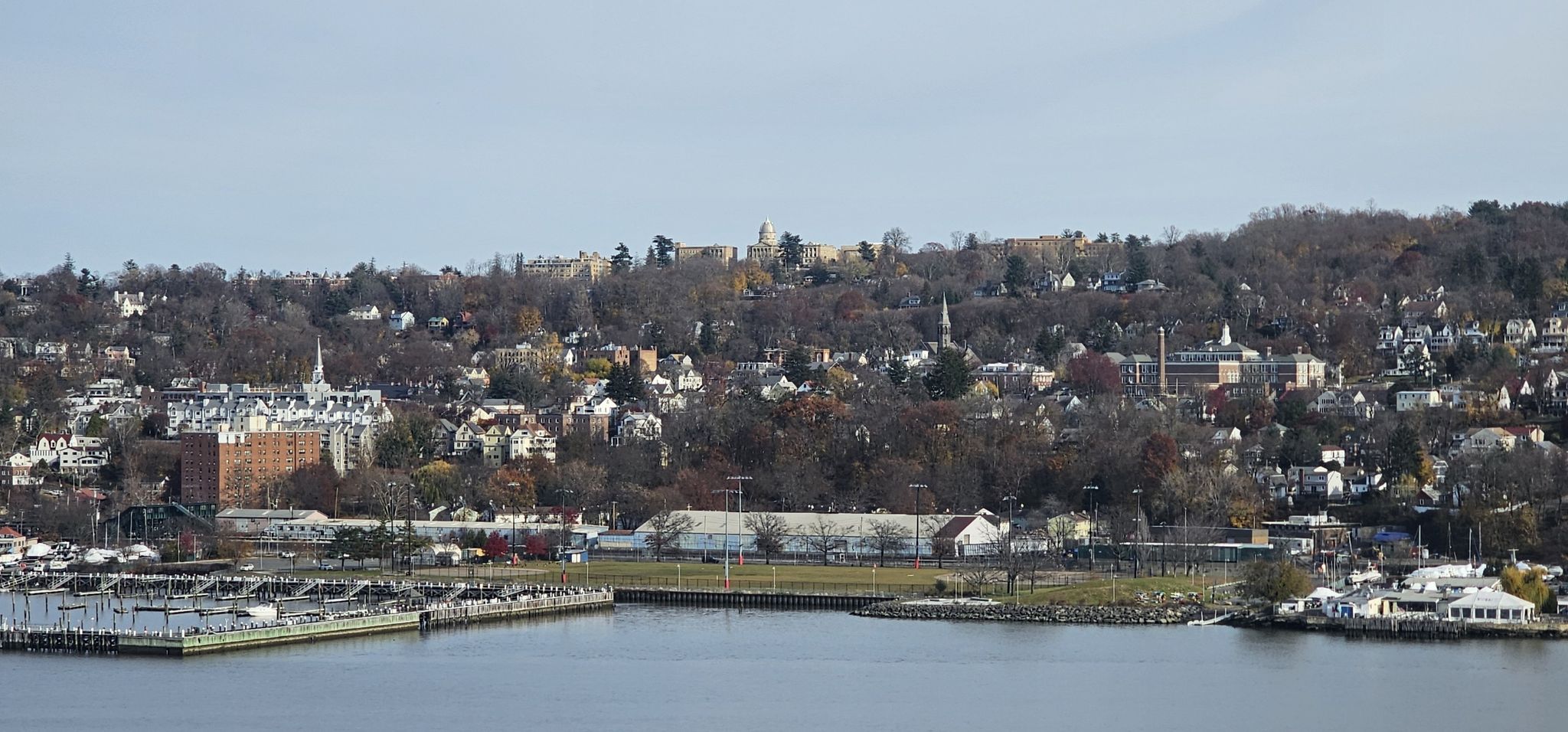 A town with buildings and trees on a hill overlooking a marina and water. - Roadbike loop from Nyack