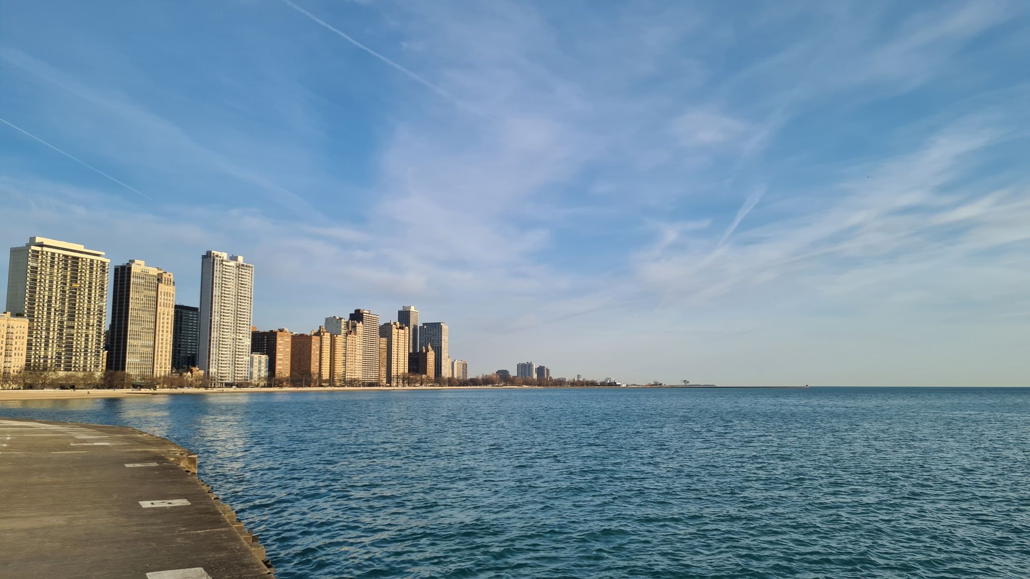 Expansive blue water next to a city skyline under a clear sky. - Lakefront Trail