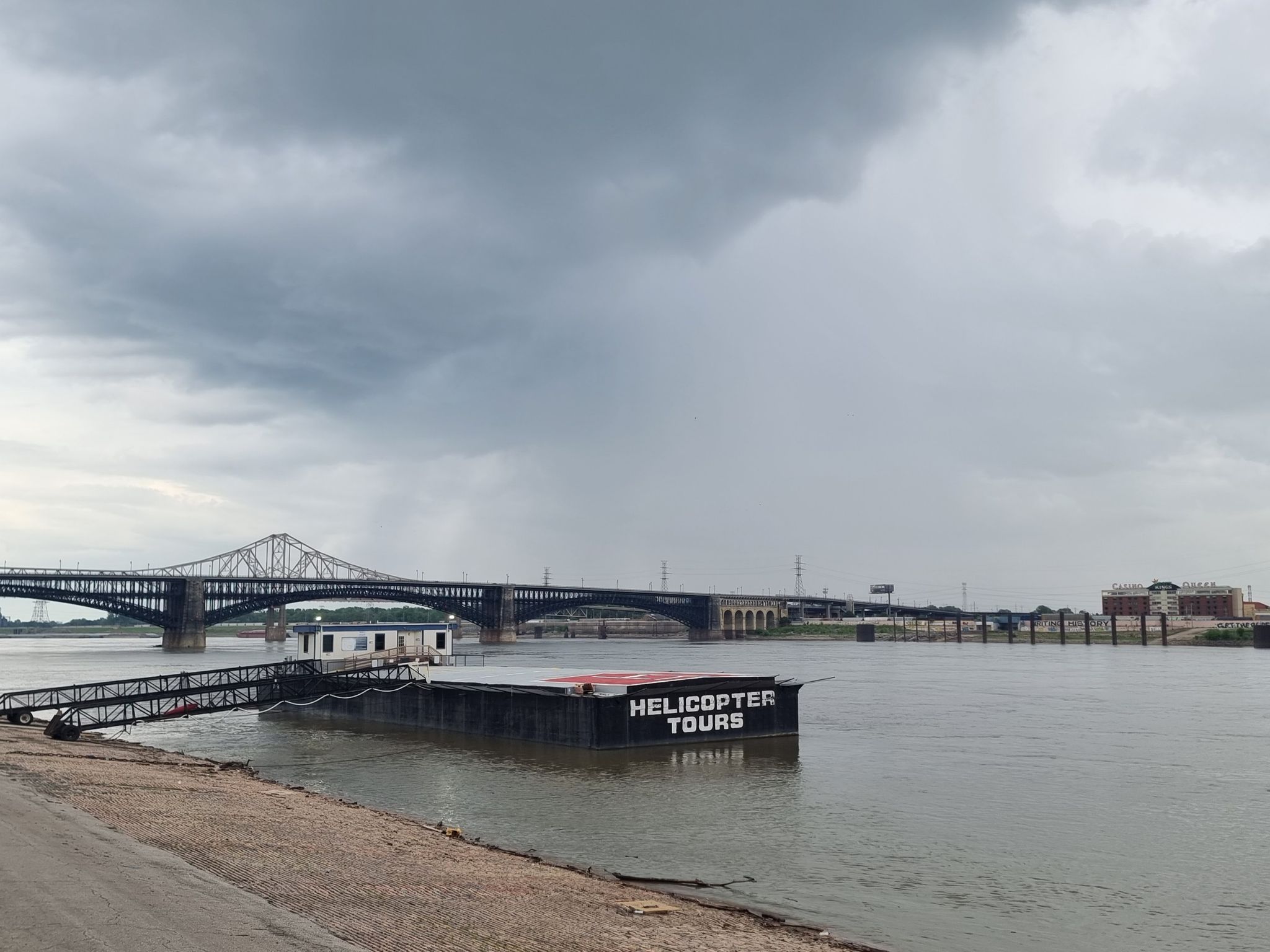 A "HELICOPTER TOURS" barge floats on a river under dark, cloudy skies. - St. Louis Riverfront Trail