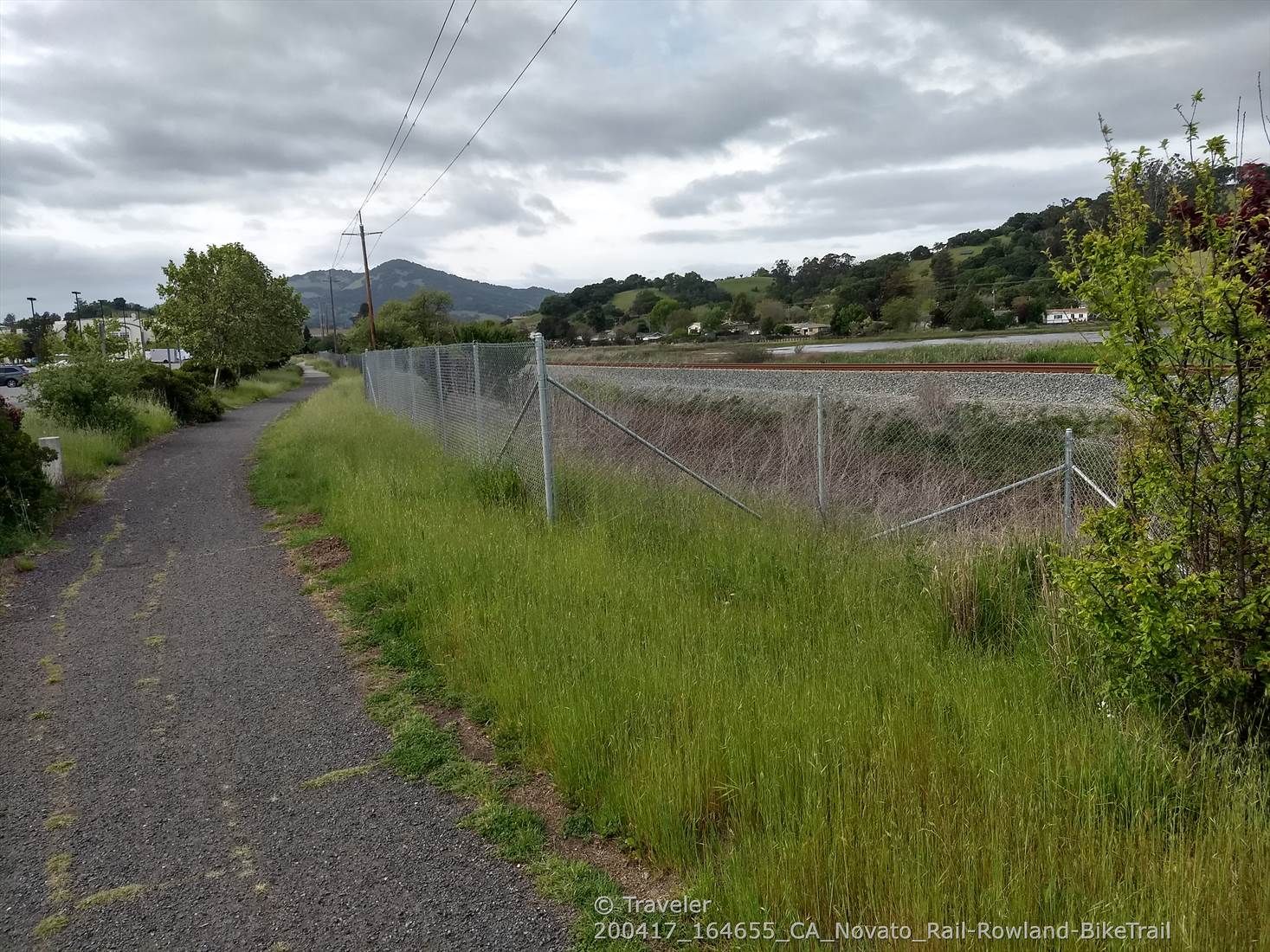 A gravel path runs alongside a chain-link fence and railroad tracks. - Old Town Novato loop via Lincoln Hill Pathway
