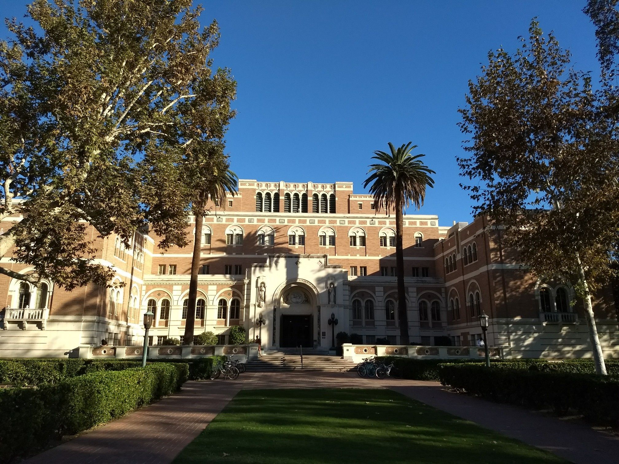 Ornate brick building with palm trees and green lawn under a clear sky. - University of Southern California and Exposition Park Walk