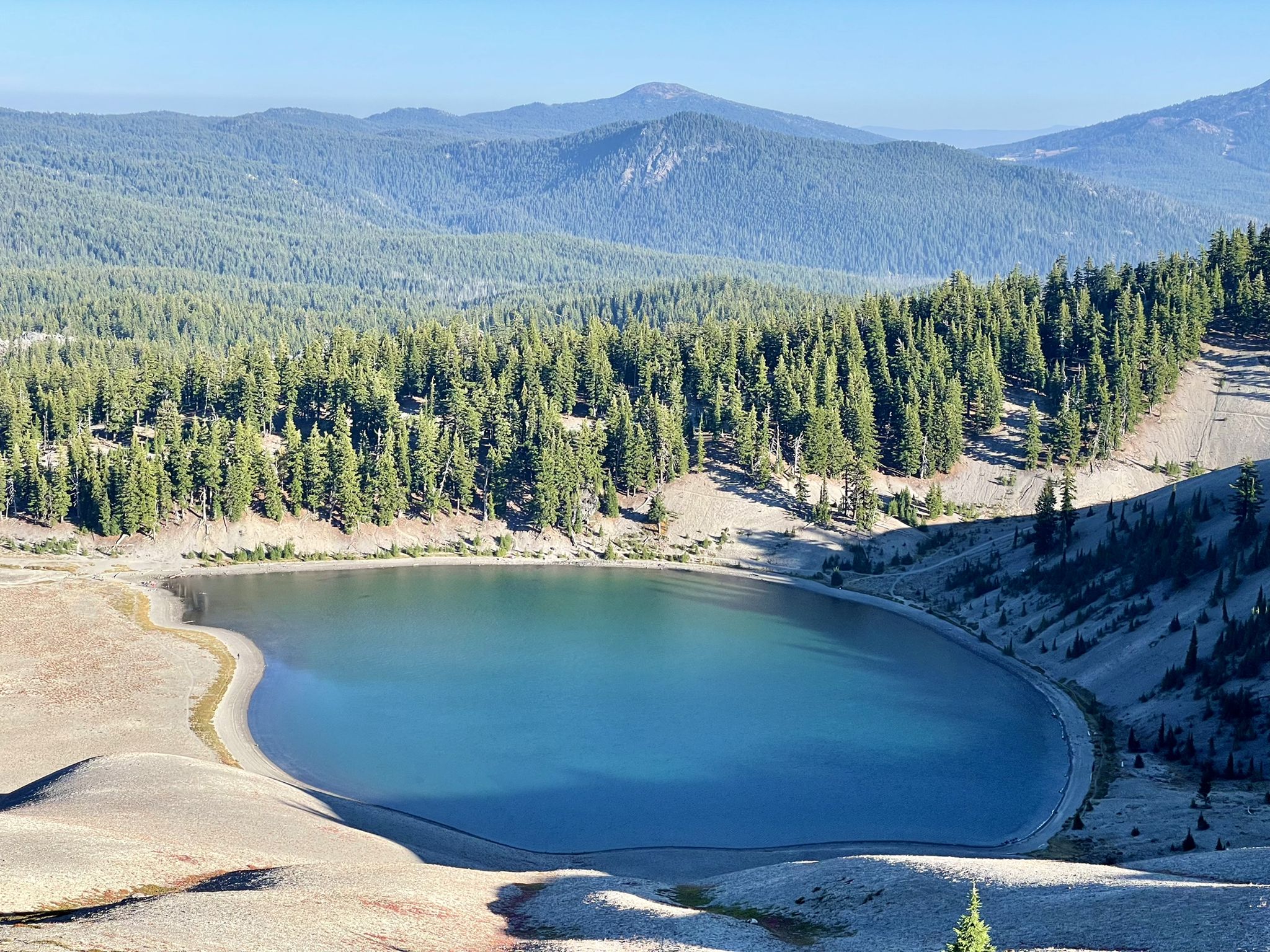 A deep blue lake surrounded by dense evergreen forests and distant mountains. - Green Lakes – South Sister Summit loop from Green Lakes Trailhead
