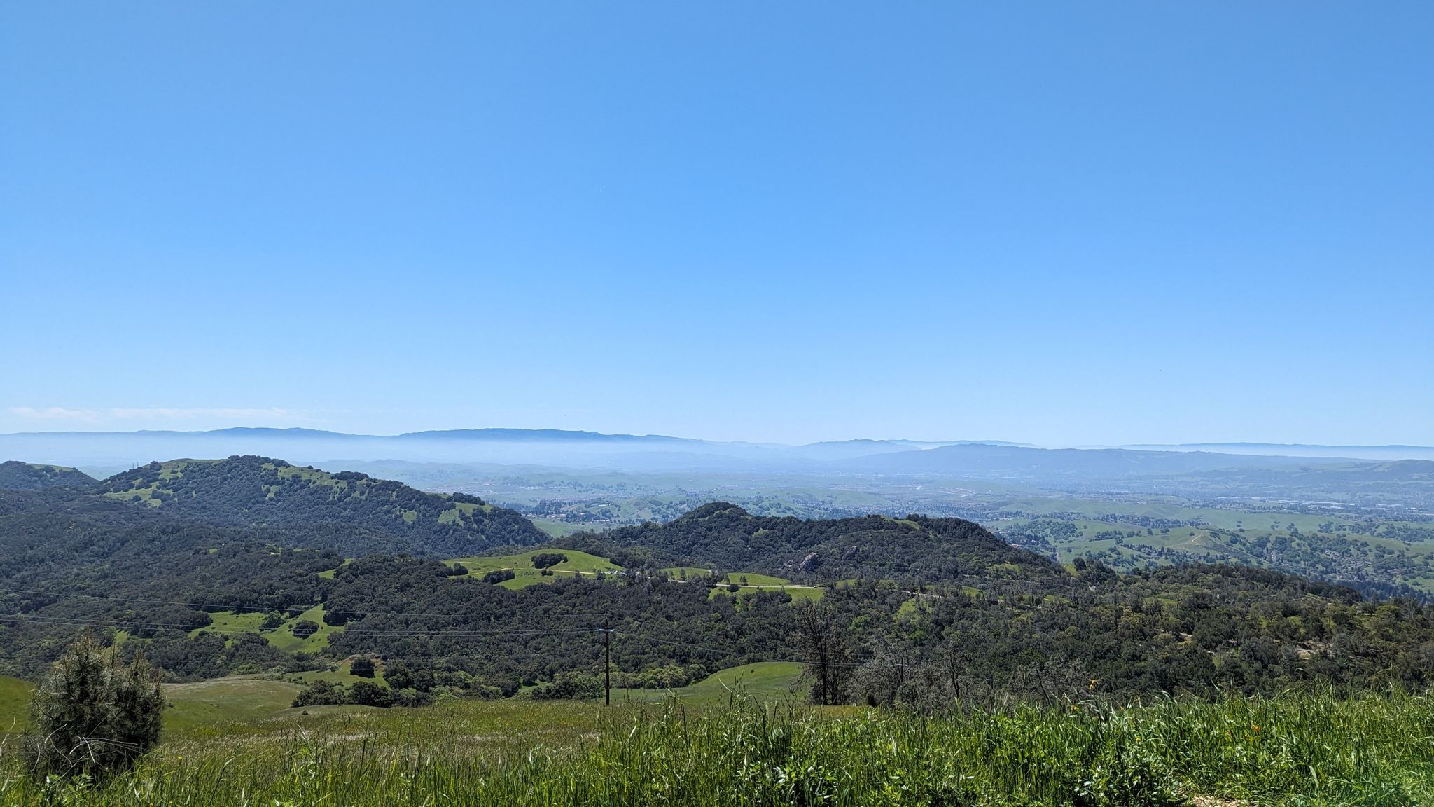 Lush green hills overlooking a hazy distant valley under a clear sky. - Curry Point – Mount Diablo Scenic Boulevard loop from Sycamore Valley Open Space Regional Preserve