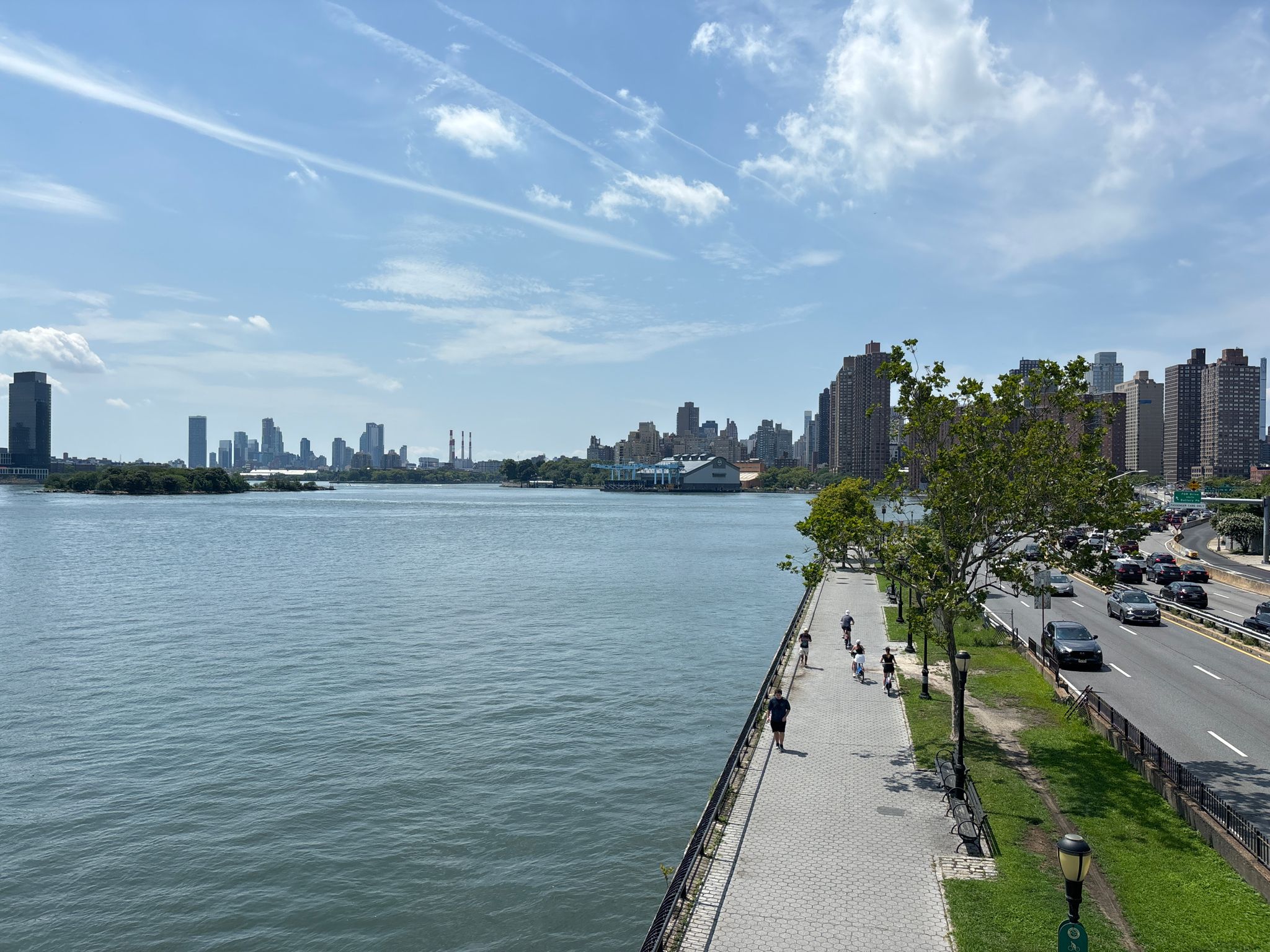 Waterfront promenade with people walking, next to a road and distant city. - Bronx Greenways and Grand Concourse Loop