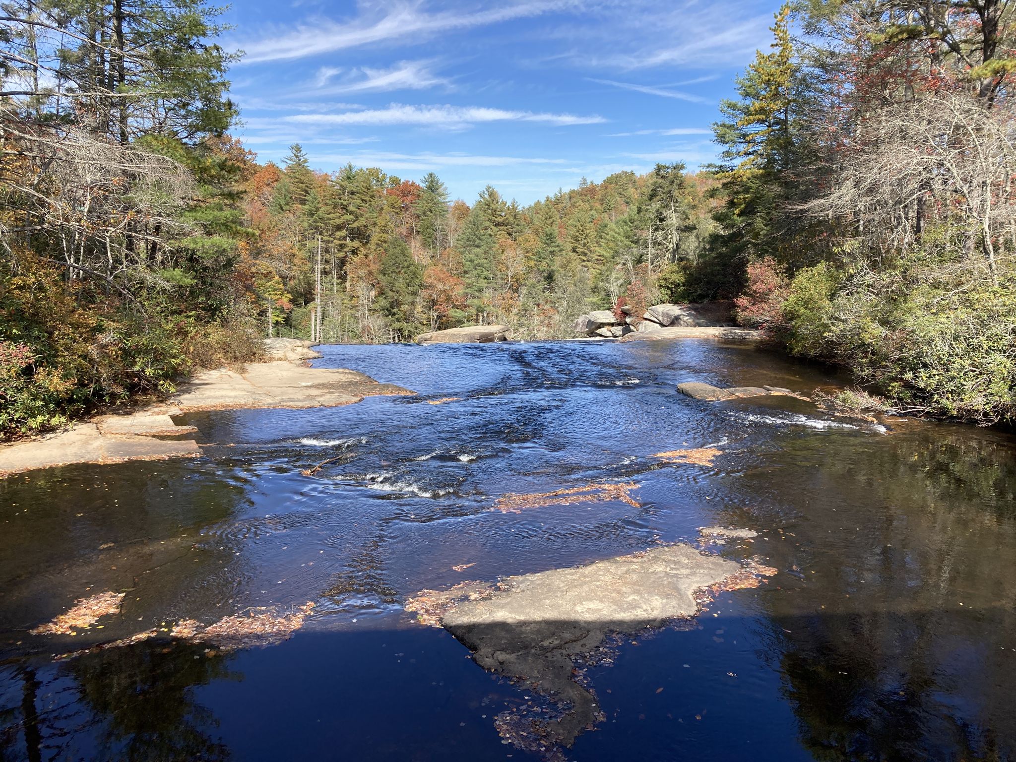 River flowing over rocks into a forest with autumn foliage under a blue sky. - Hooker Falls, Triple Falls, Bridal Veil Falls, and High Falls Trail