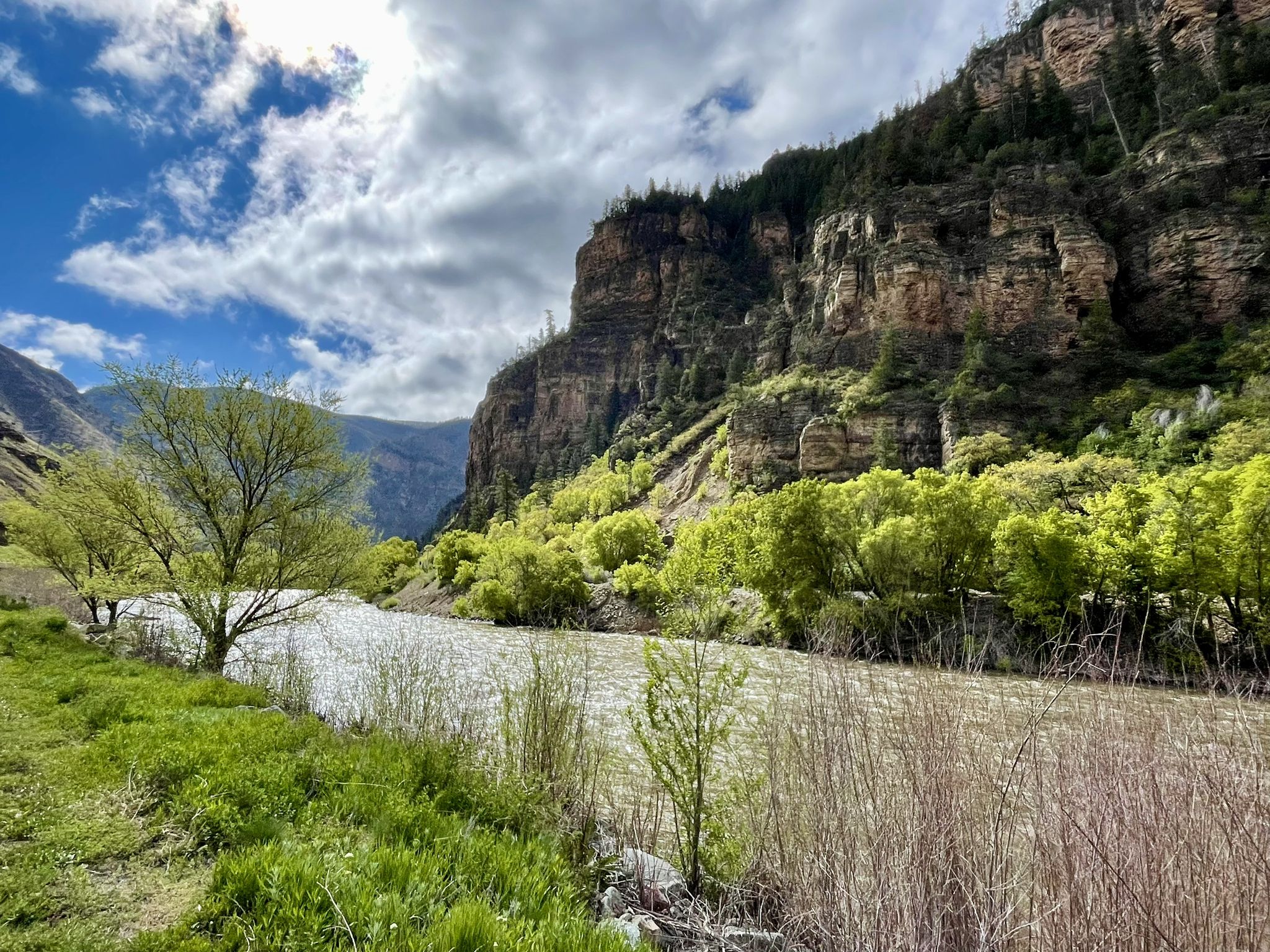 River flowing through a canyon with steep, forested cliffs under a cloudy sky. - Glenwood Canyon Recreation Trail