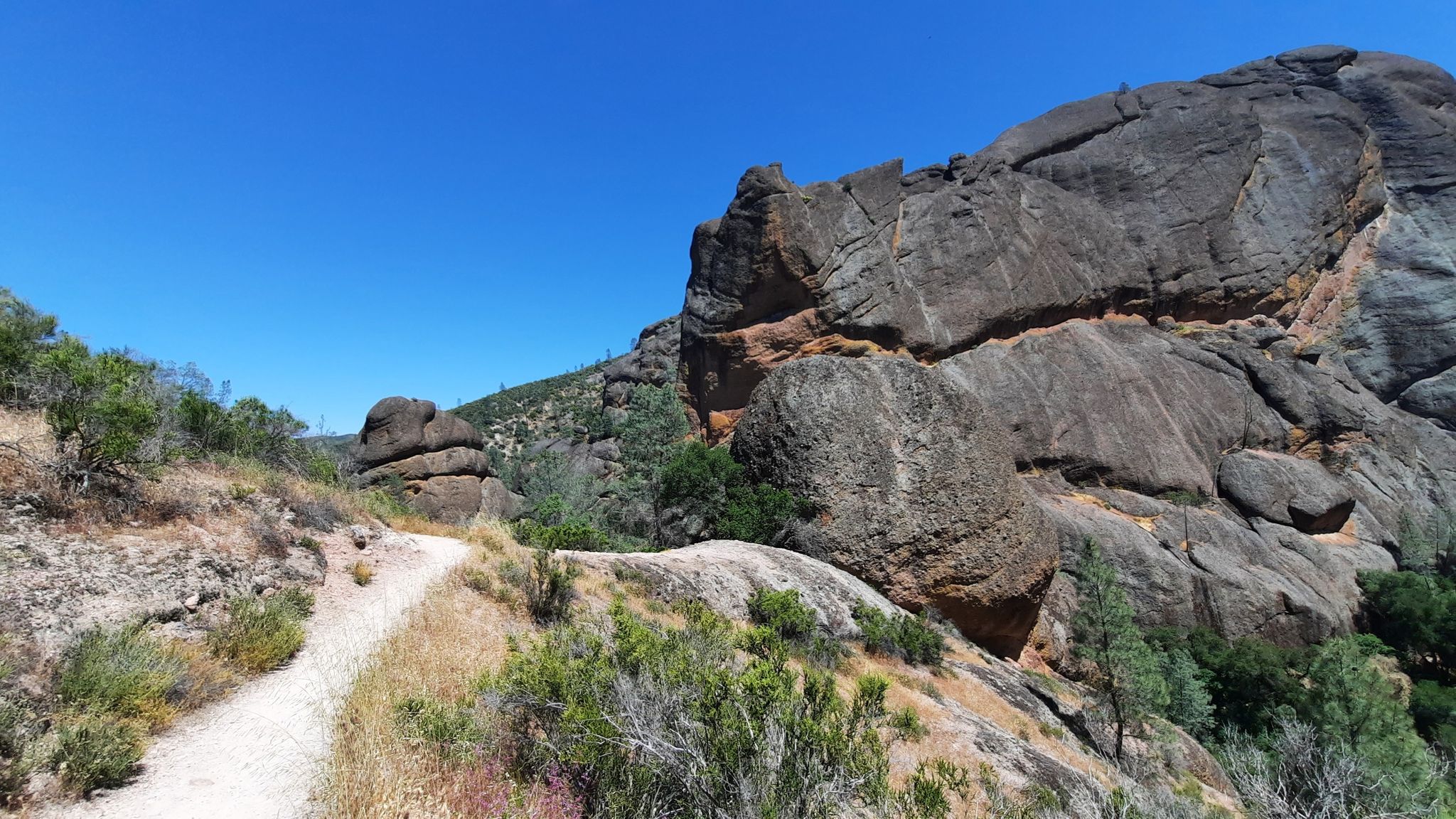 Dirt path winding alongside massive rock formations under a clear blue sky. - Balconies Caves – Bench Trail – Southern Section loop from Shuttle Bus Stop